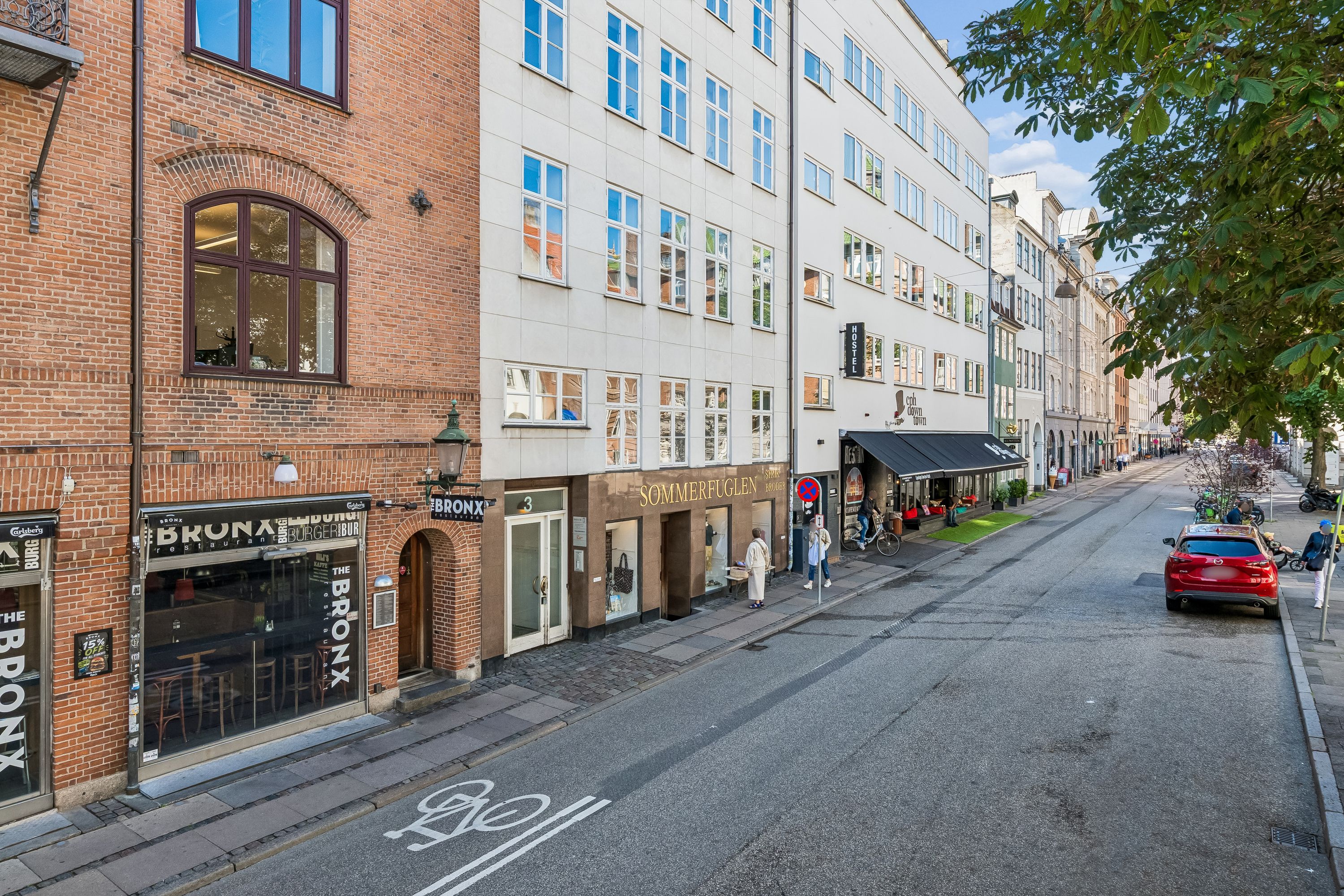 Kontor på Vandkunsten 3 med cafeer og forretninger på gaden og en rødmalet bil parkeret på siden af gaden