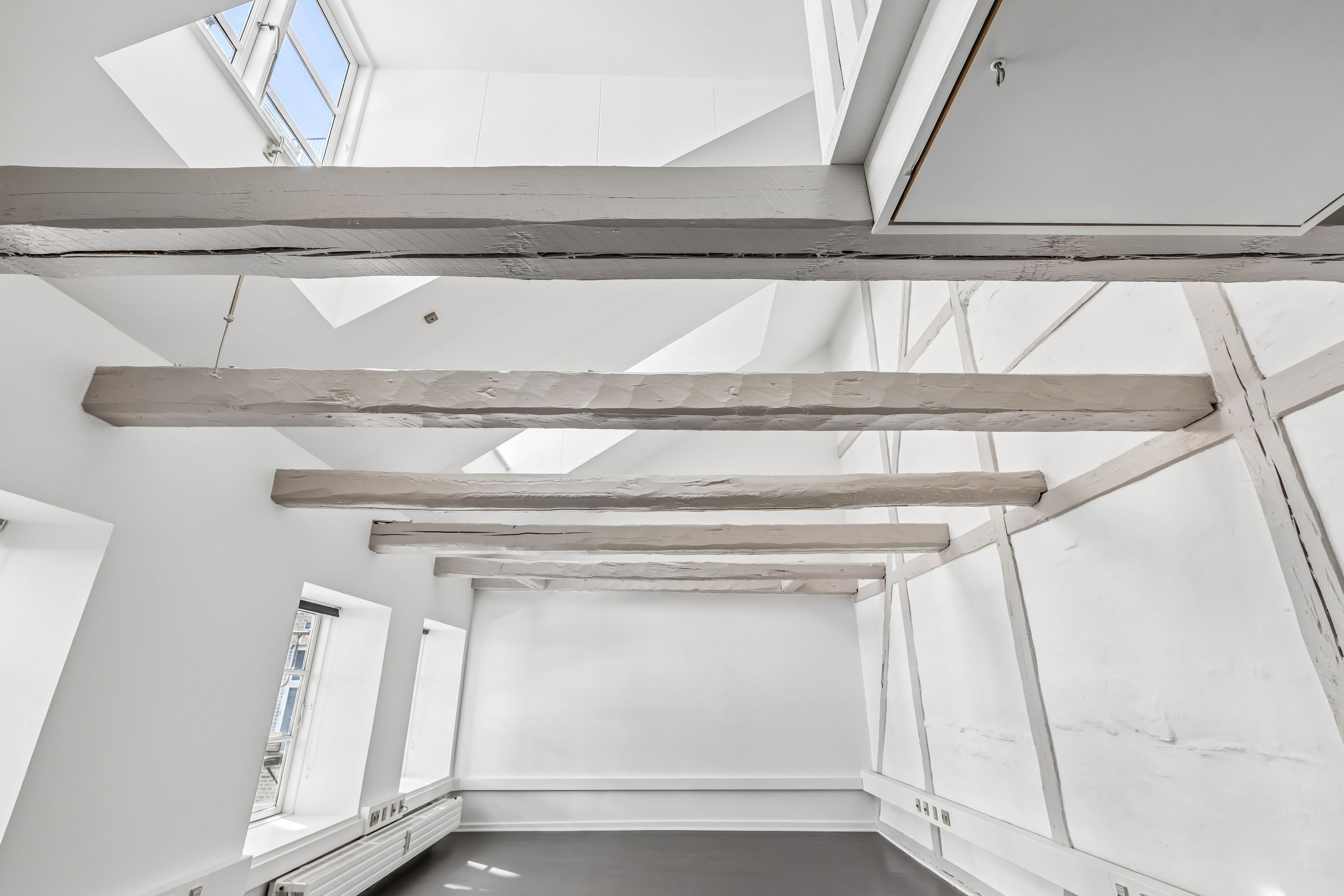 Lyst kontor med højt loft og lyse vinduer samt lyse og hvide vægge og træbjælker