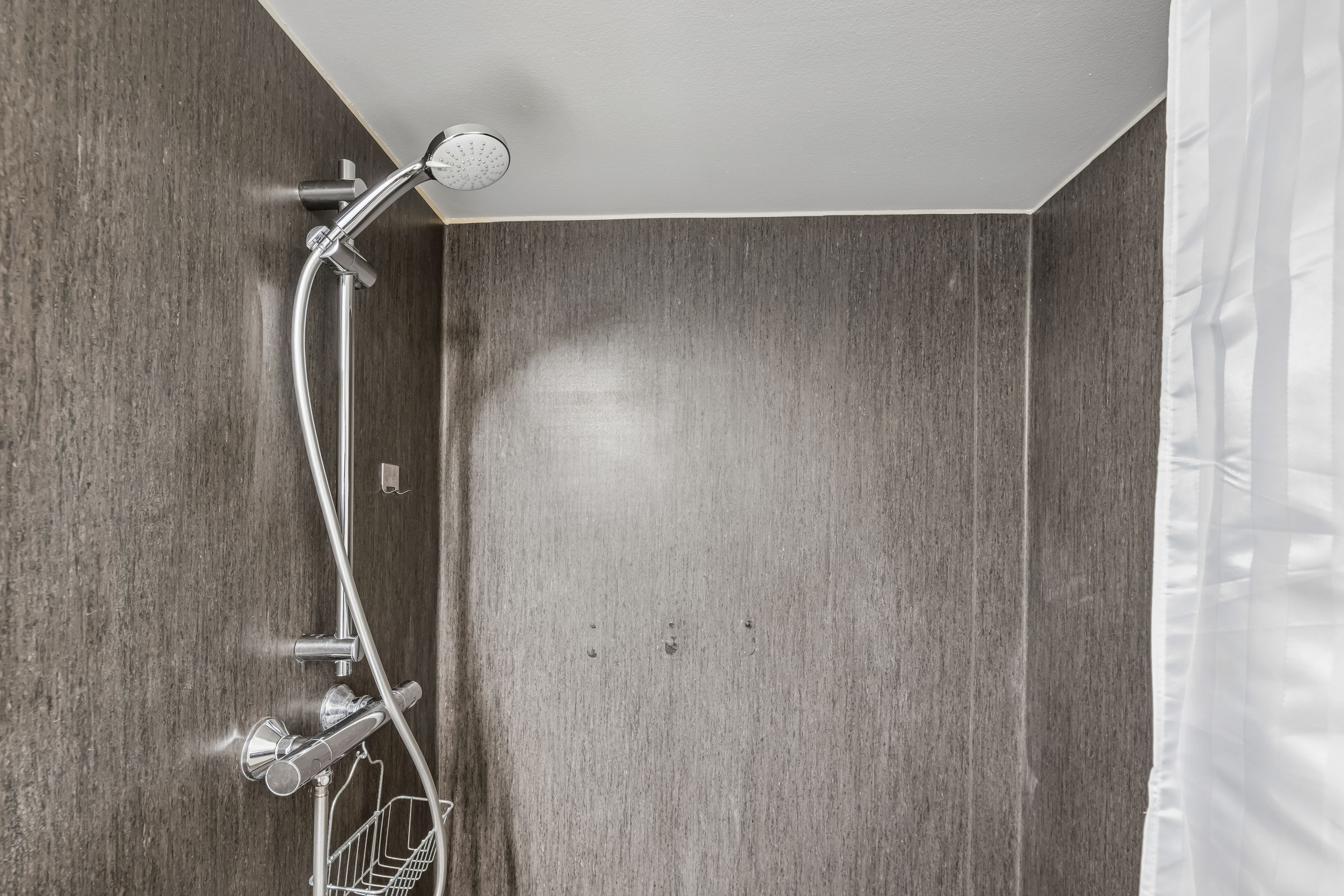 En lys og elegant brusekabine med moderne design og en hængende metalkurv for opbevaring af badeprodukter