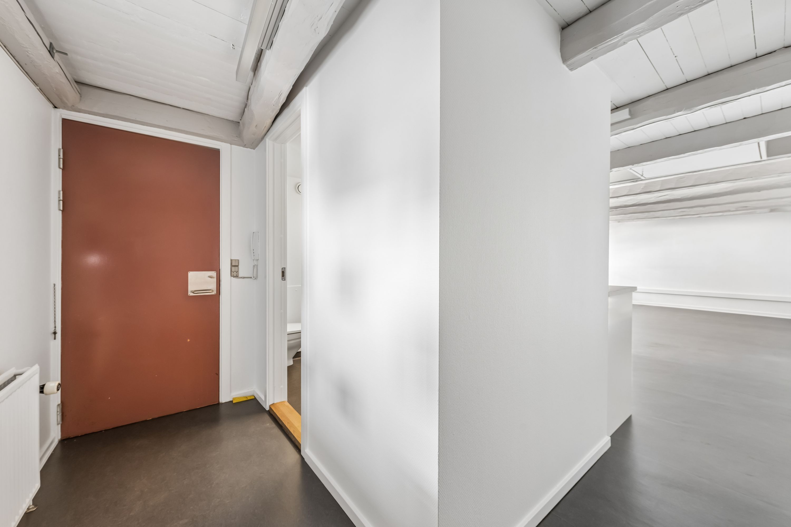 Kontorlokaler med moderne design og lyse lofter, hvor en dør fører til toilettet og en radiator sidder på væggen
