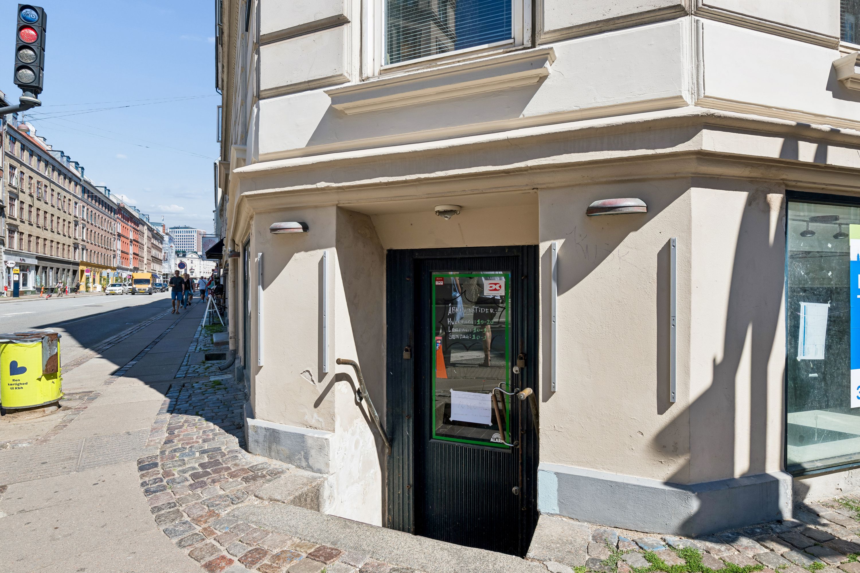 En erhvervsandel til salg på Vesterbrogade 101 i København V. Døren til ejendommen er lukket og har tekst og vinduer med skrift på. Der er trafiklys på gaden