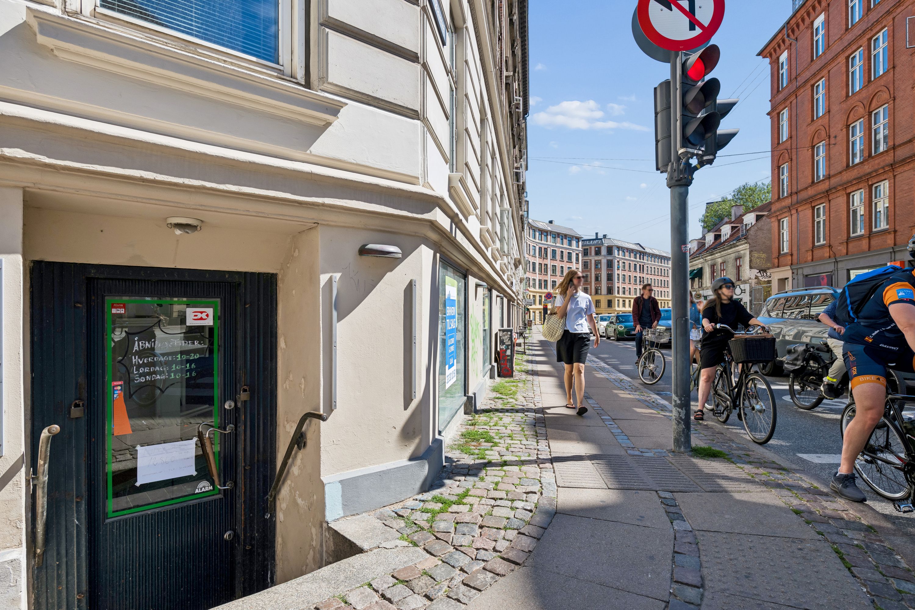 Københavnsk gadestrøg med to cyklister og to fodgængere, vinduer og gamle bygninger, erhvervslokaler, skilte og trafikregulatorer