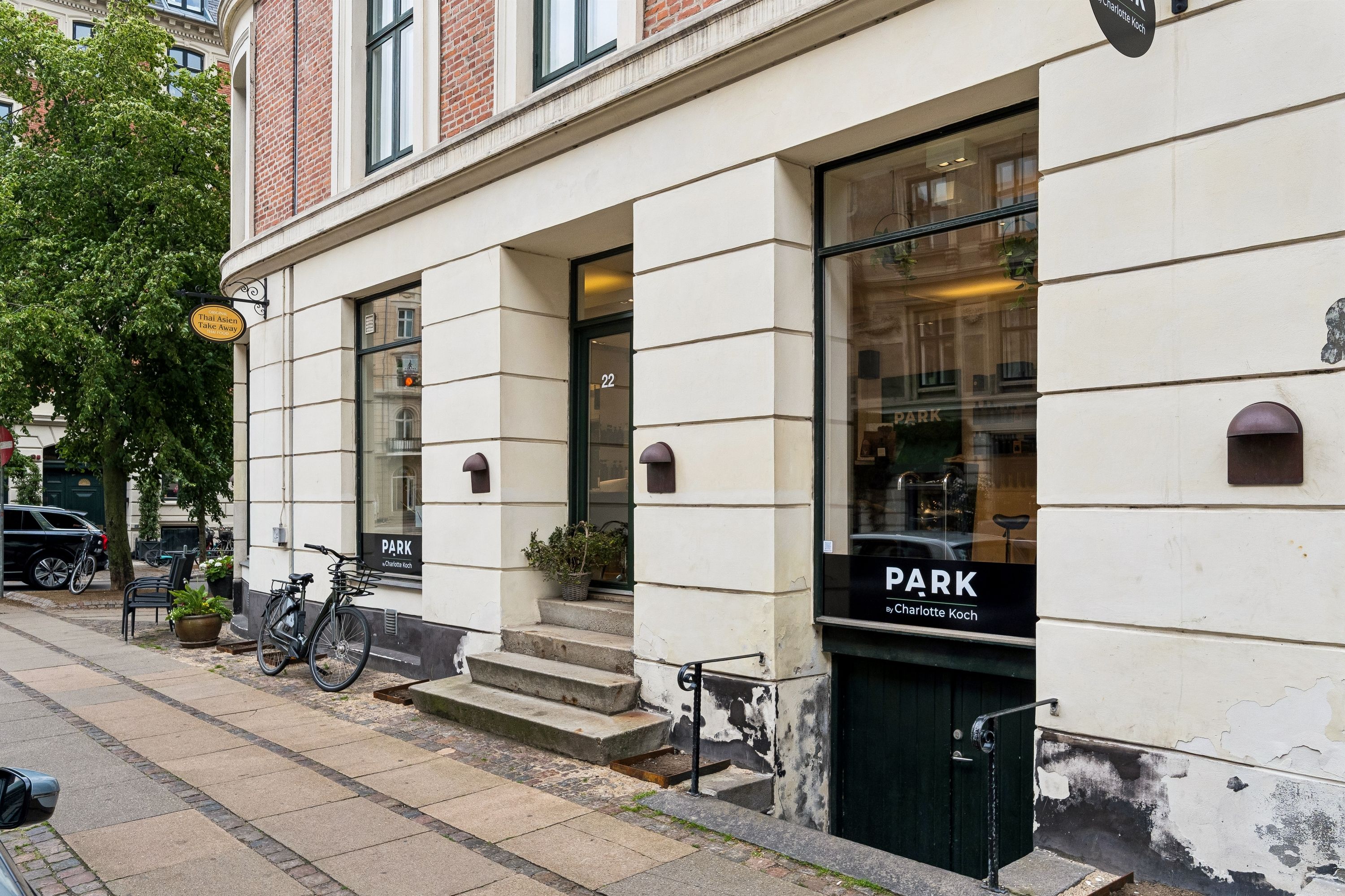 Butik med grønne døre og "Park"-skilt på Holbergsgade 22 i København. To cykler står parkeret foran indgangen. En potteplante og et bord med stole er udenfor.