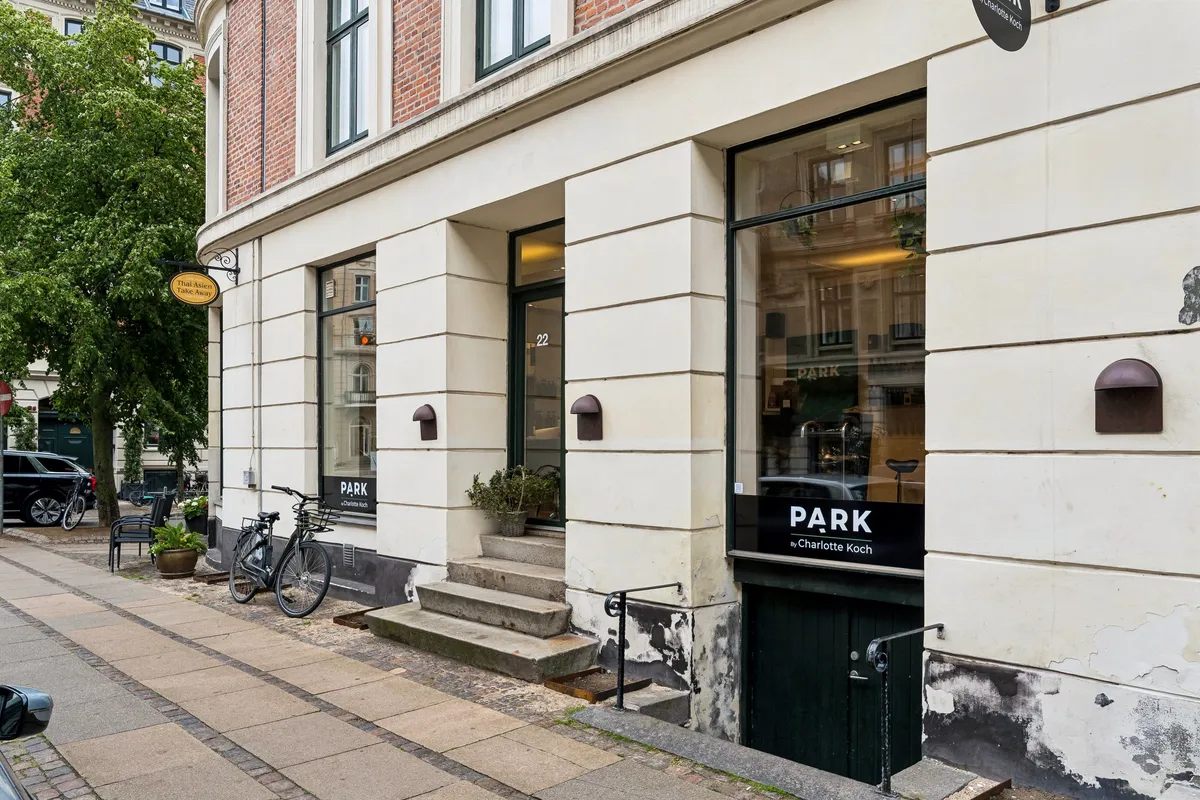 Butik med grønne døre og "Park"-skilt på Holbergsgade 22 i København. To cykler står parkeret foran indgangen. En potteplante og et bord med stole er udenfor.