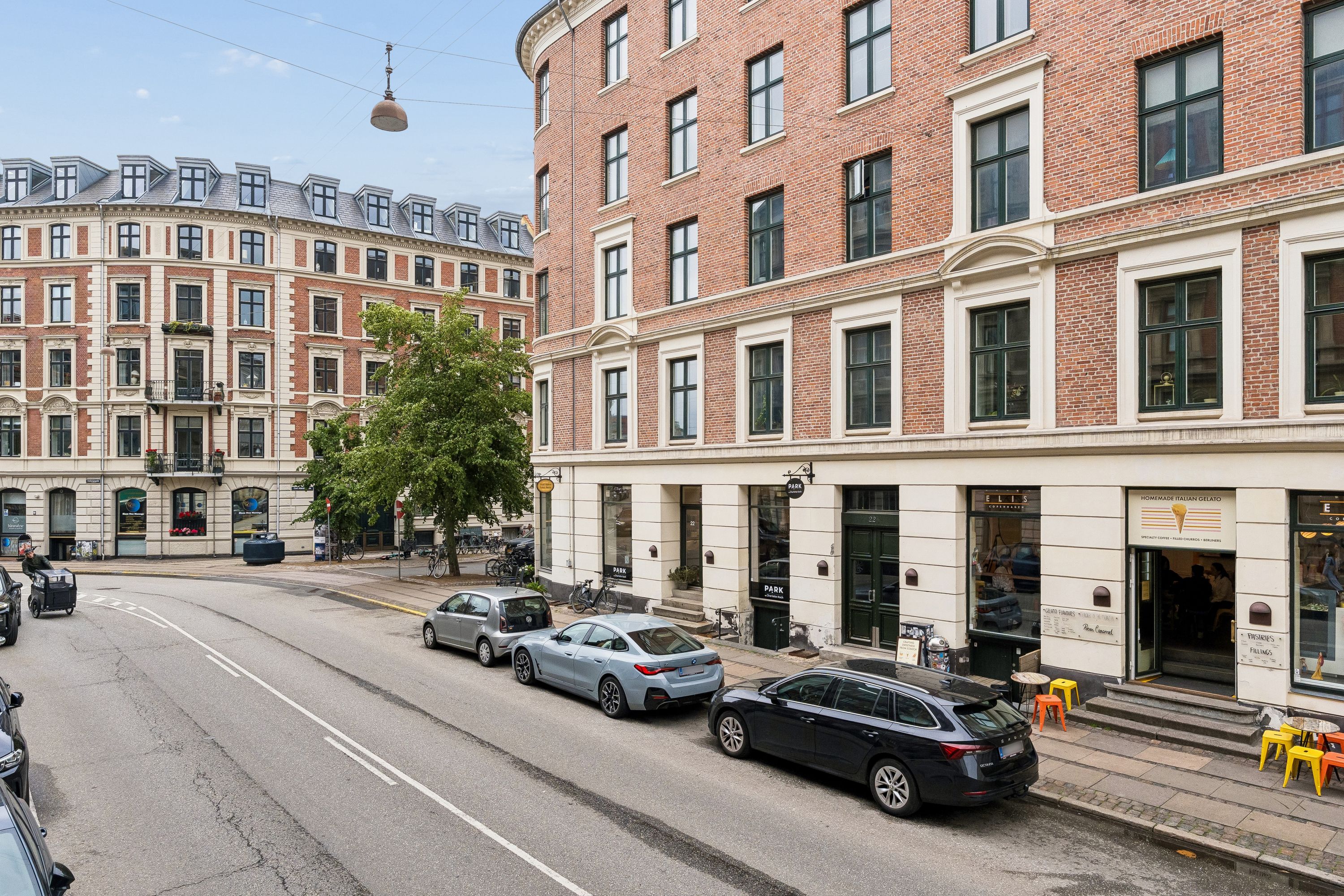 Flere biler parkeret på Holbergsgade og foran bygningen er der flere stolpeborde med is og cafeen Ellis Coffeehouse