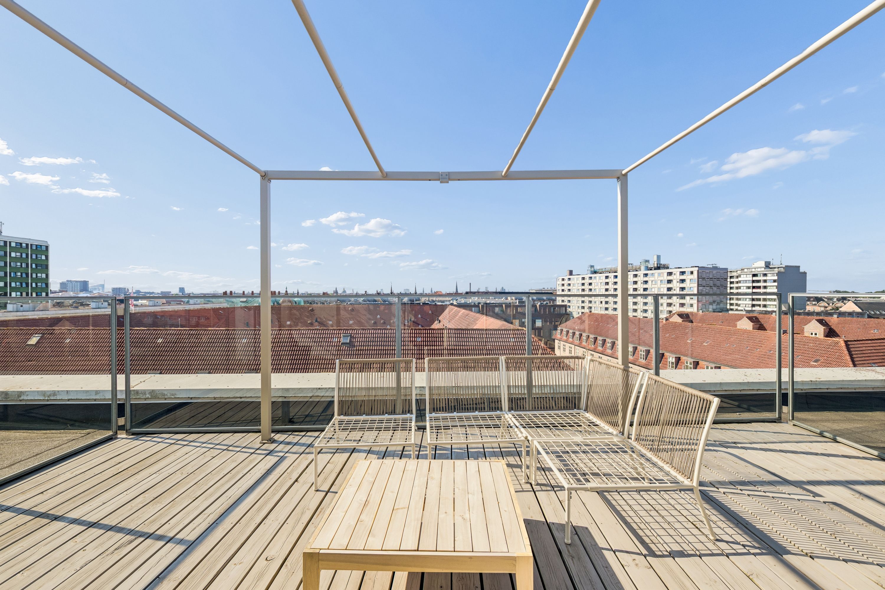 Kontor til leje med udsigt til Københavns bygninger og himlen. Solrige, åbne rum med moderne møbler og trægulv. Elegant design med lyse metalstrukturer og glas.