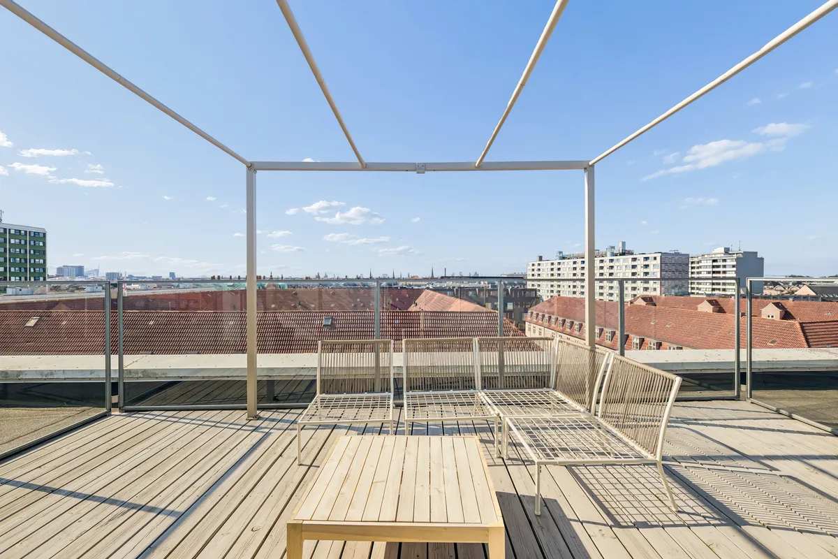 Kontor til leje med udsigt til Københavns bygninger og himlen. Solrige, åbne rum med moderne møbler og trægulv. Elegant design med lyse metalstrukturer og glas.