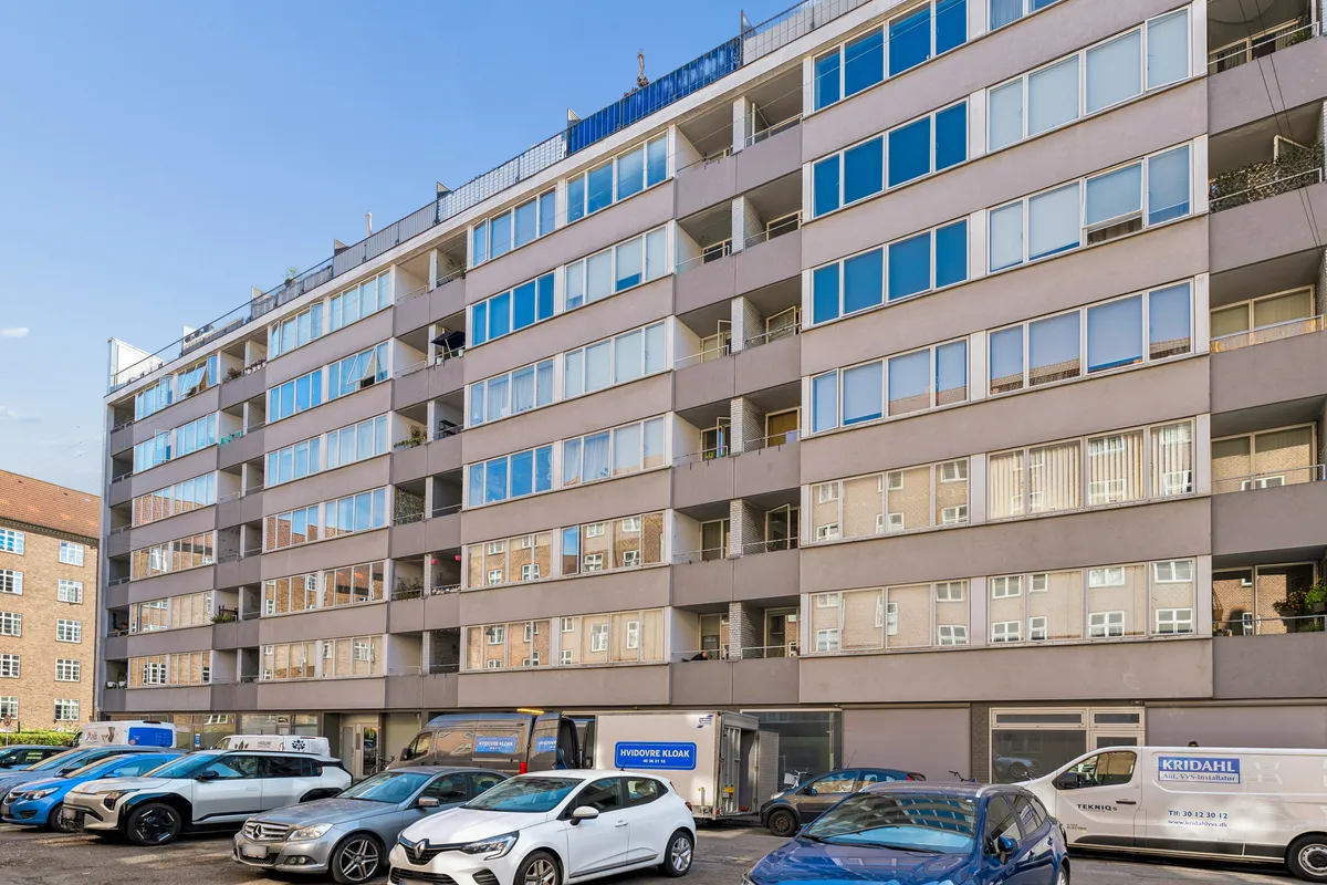 Hvid og blå kontorblok med flere biler parkeret udenfor på Østerbrogade 113 i København. Tre hvide og en blå bil parkeret i rækker udenfor.