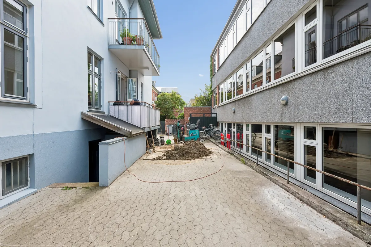 Kontor til leje med terrasse, have og parkeringsplads. Bygningen har flere vinduer og balkoner. Arbejdsmaskiner og jord på gaden. Bygningen ligger i en smuk bydel.