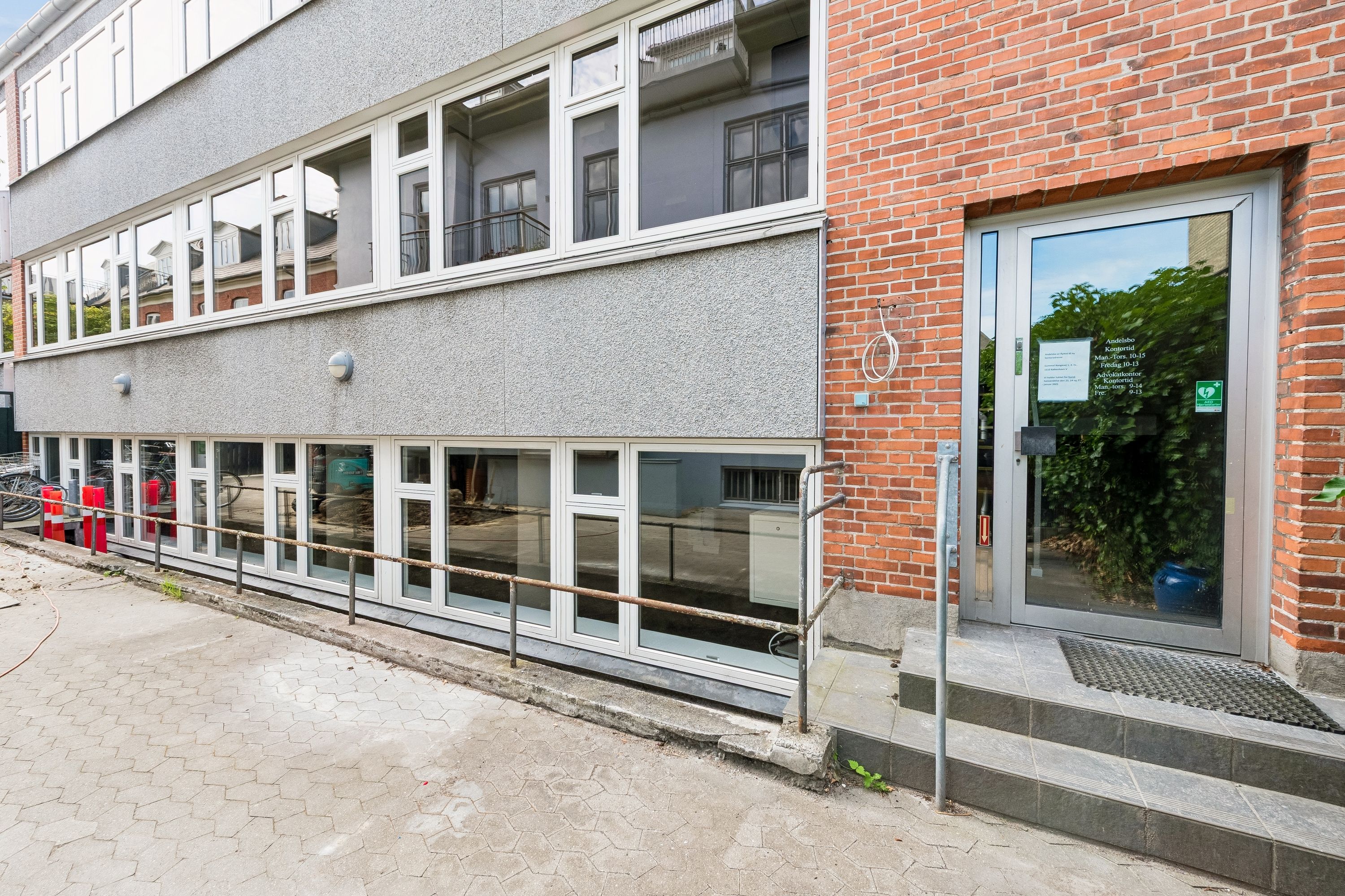 Kontor med glasdøre og vinduer på Dronning Olgas Vej 37A i Frederiksberg, indgangen har trin og skrapelister, røde og hvide bøsser og et grønt plantekar i vinduet