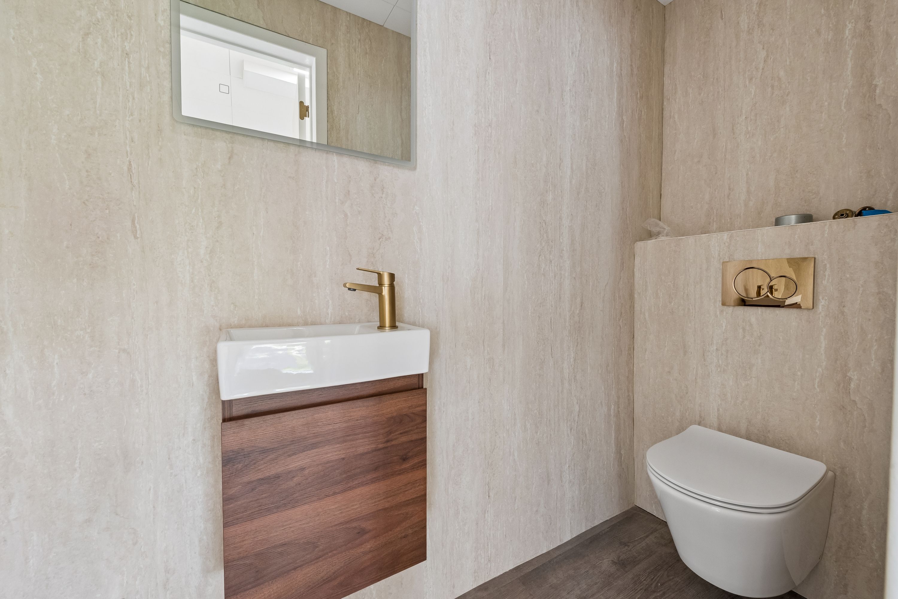 Modernt design med gulvbelægning og belysning samt en stor spejl, hvidt toilet og vandhaner med bronzefarvet finish