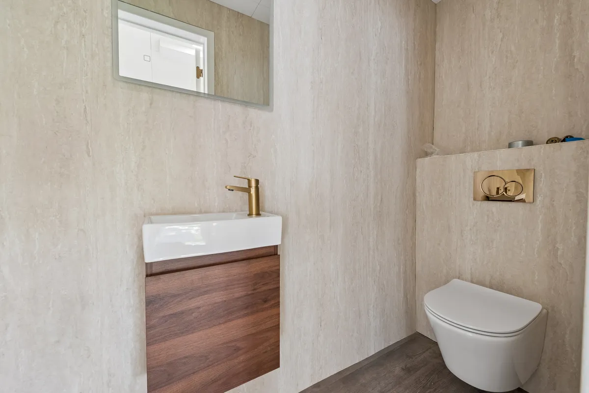 Modernt design med gulvbelægning og belysning samt en stor spejl, hvidt toilet og vandhaner med bronzefarvet finish