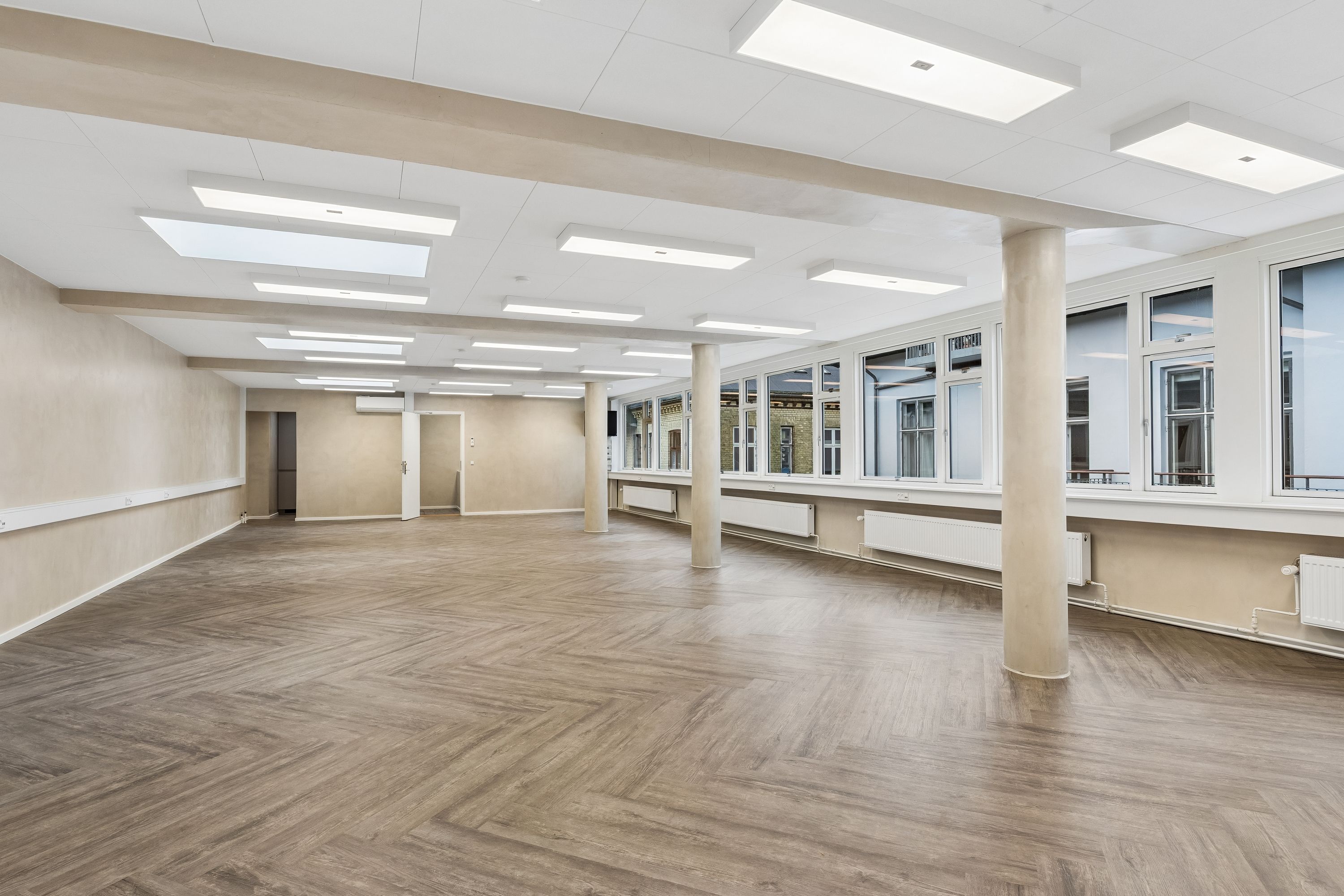 Kontor til leje i Frederiksberg med lyse loftslamper, trægulve og store vinduer. Moderne og indflytningsklart lejemål med højt til loftet og udsigt til gaden