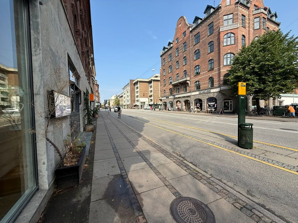 Frederiksberg bymidte med cykelspor og gågade, med en person på cykel og gående folk og en grøn søjle med skilte på hjørnet