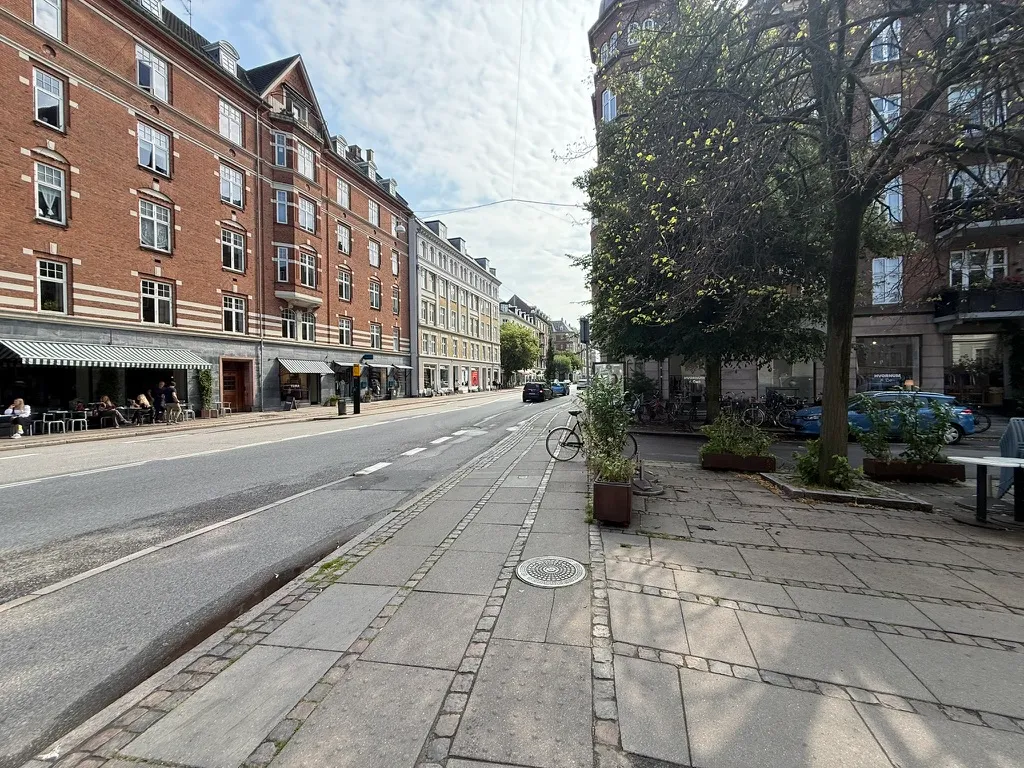 Take-away og bageri ligger på Gammel Kongevej 107. Både cykler og biler er parkeret langs gaden. Få mennesker sidder på terrassen med deres drikke og mad.