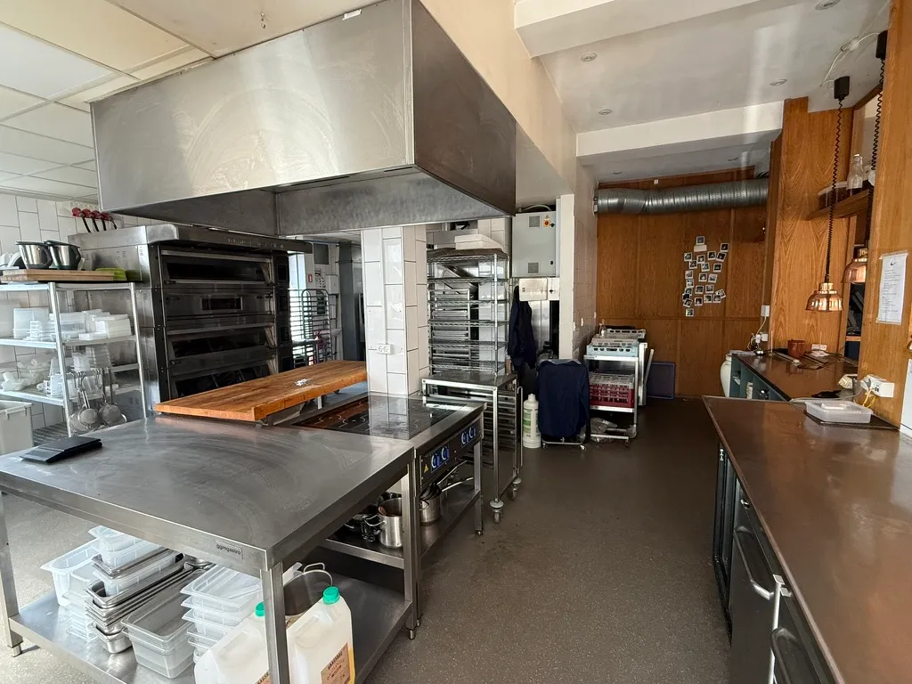 En stor, nyrenoveret bagerikedel i Frederiksberg med moderne køkkenudstyr og apparater, flere ovne, et stort køkkenbord, og flere lagerhylder med mad og ingredienser