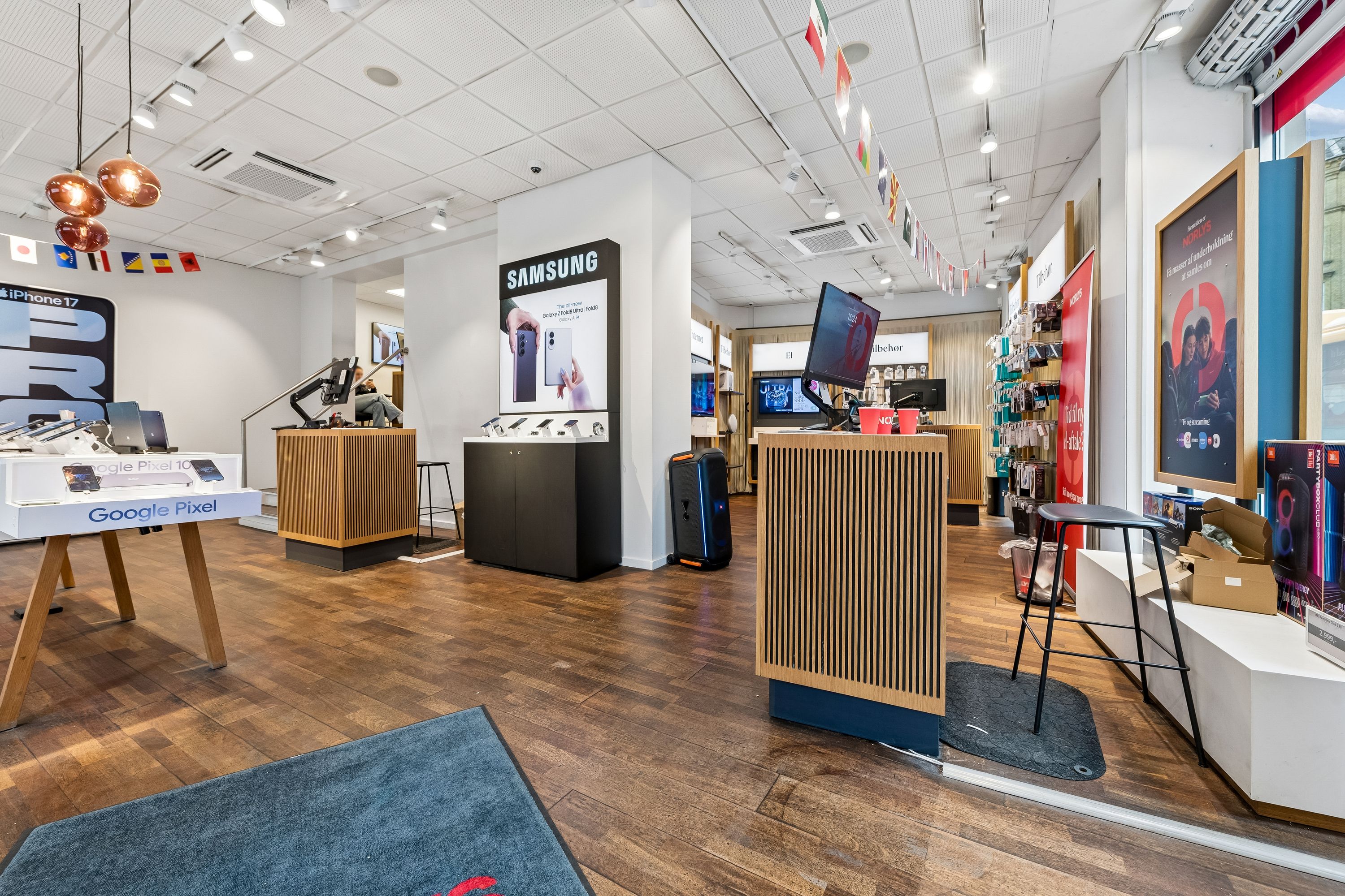 En butik med Samsung og Google Pixel produkter i en moderne indretning med lyse loftslamper, trægulv og flag på væggen