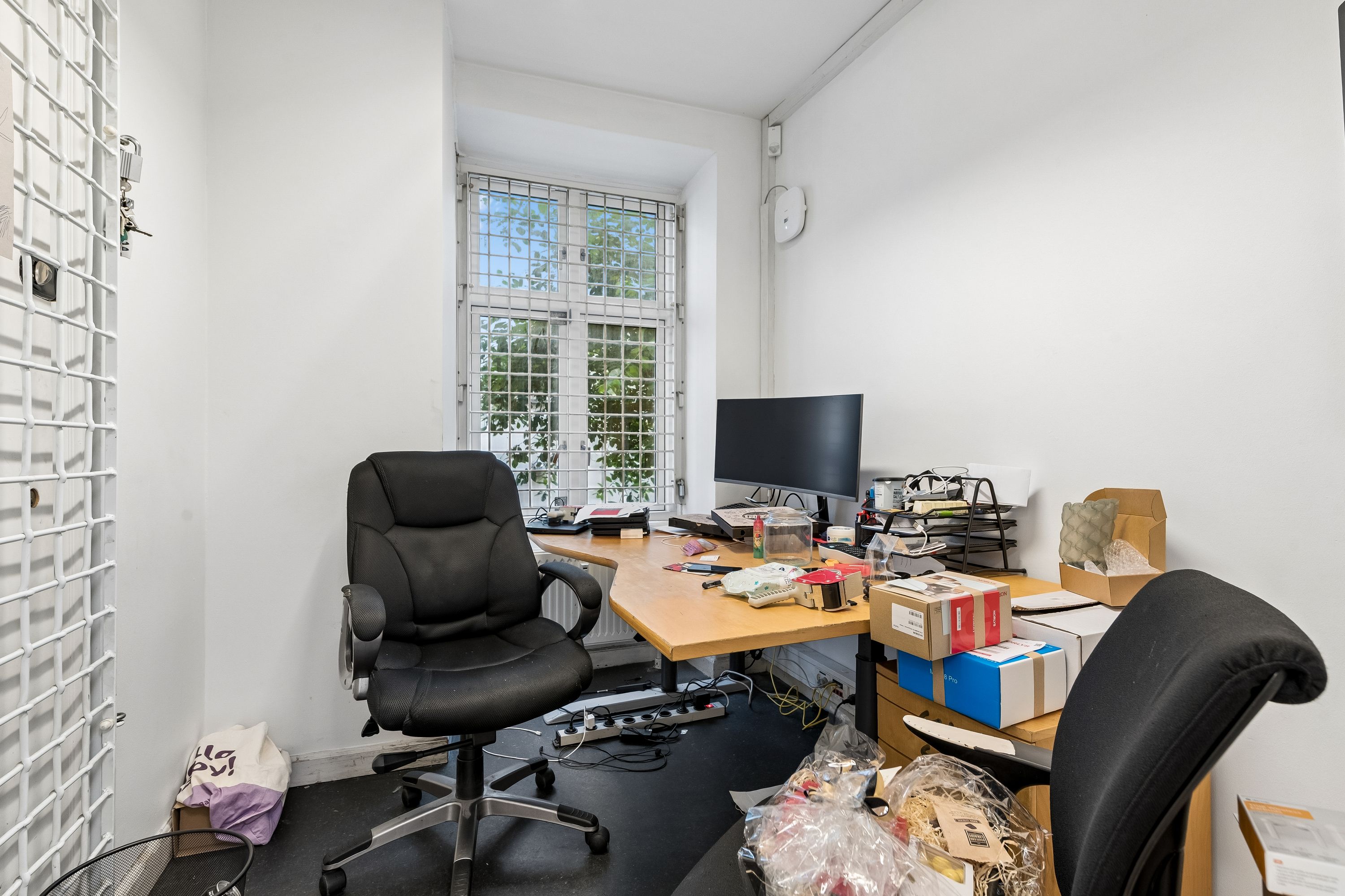 Billede af en tom kontor, med skrivebord og stole. Skrivebordet er fyldte med papkasser og computerudstyr, mens stolerne står tomme.
