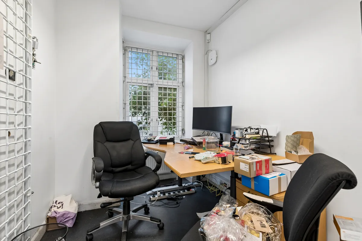 Billede af en tom kontor, med skrivebord og stole. Skrivebordet er fyldte med papkasser og computerudstyr, mens stolerne står tomme.
