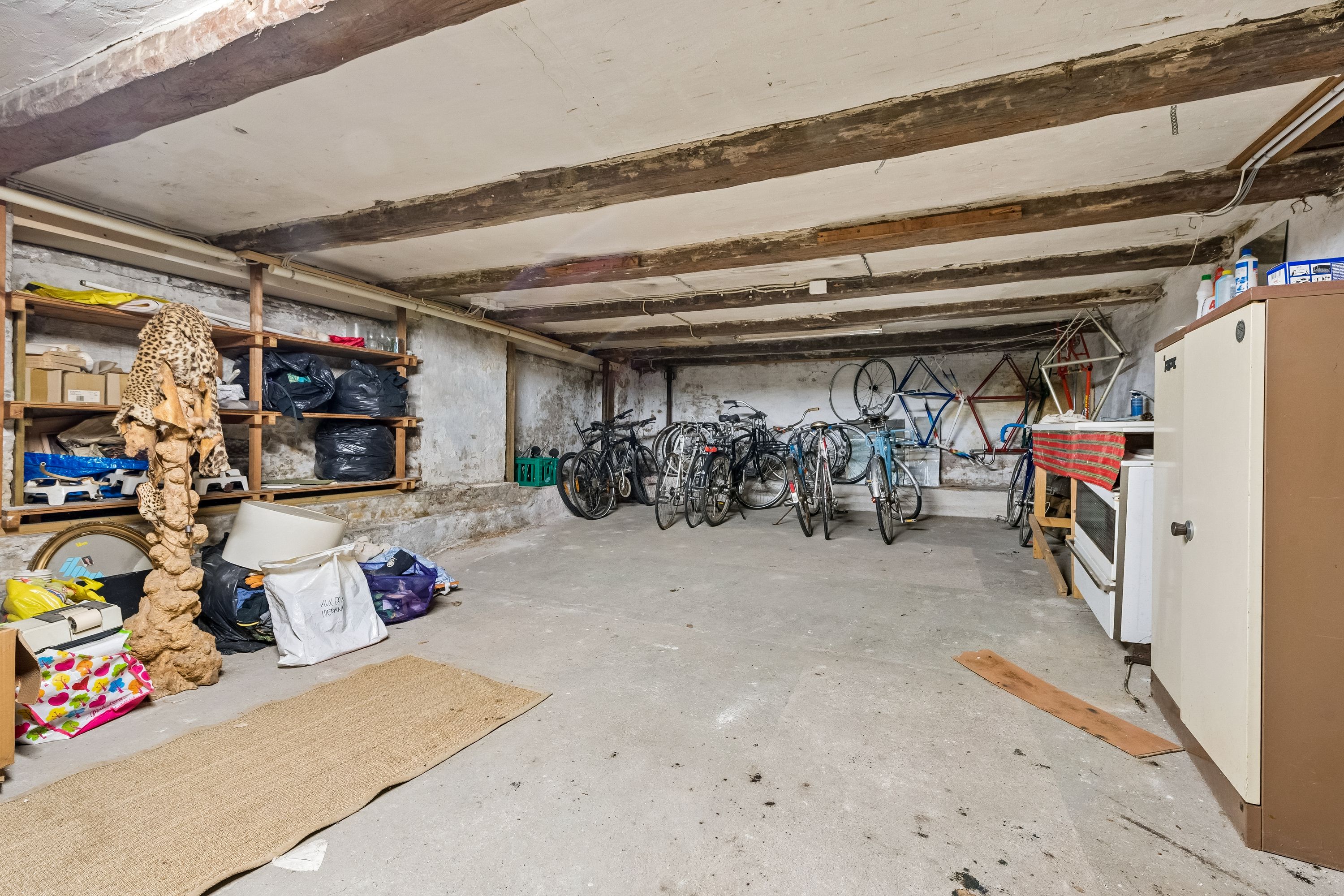 Kælder med lagerrum, hvor der er parkeret flere cykler, en ovn og diverse lagerreoler med sager