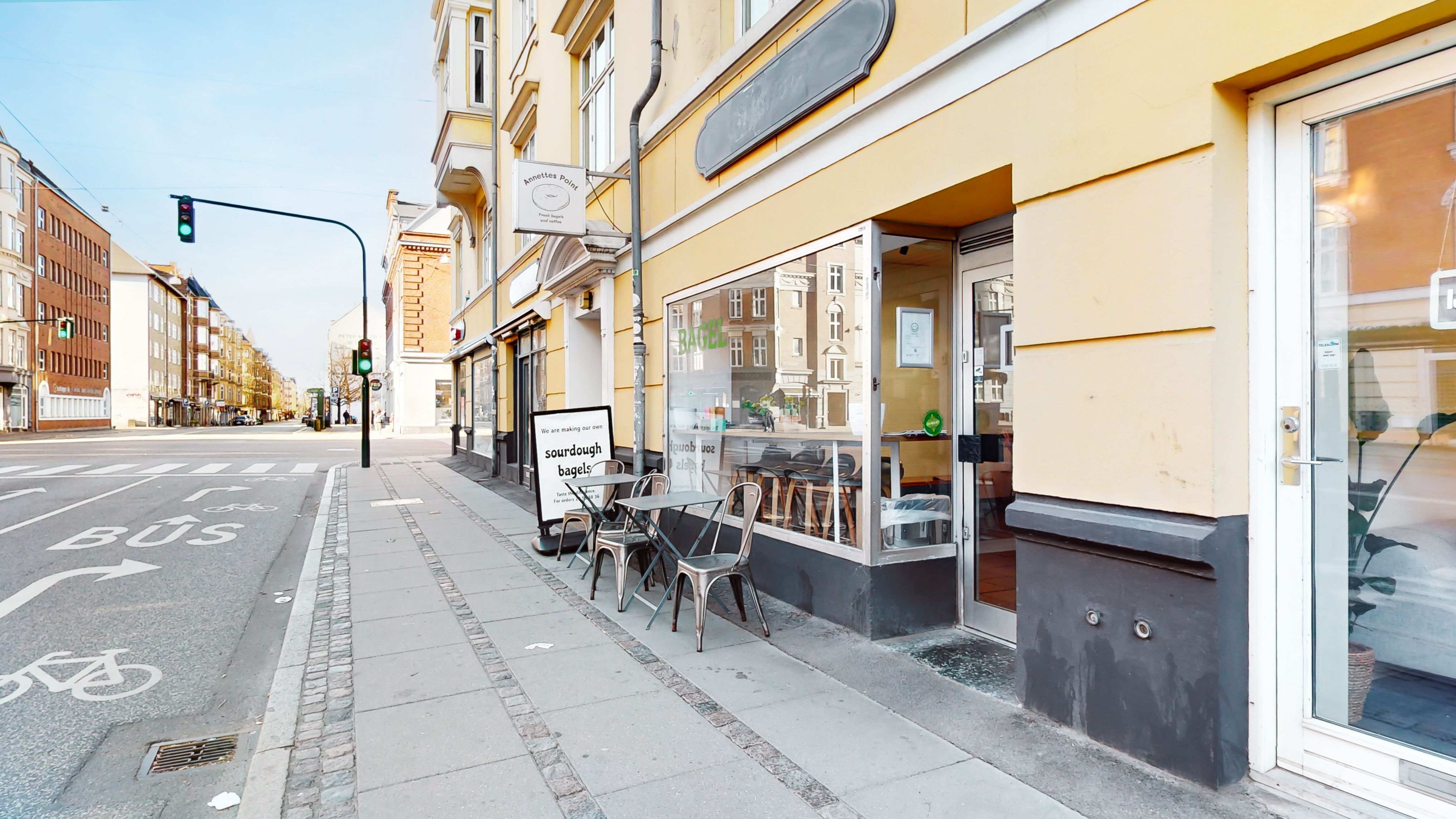 En café med tegning om surdegsbagle står på hjørnet af en gade med busstribe og cykelstribe, der er beklædt med gult.