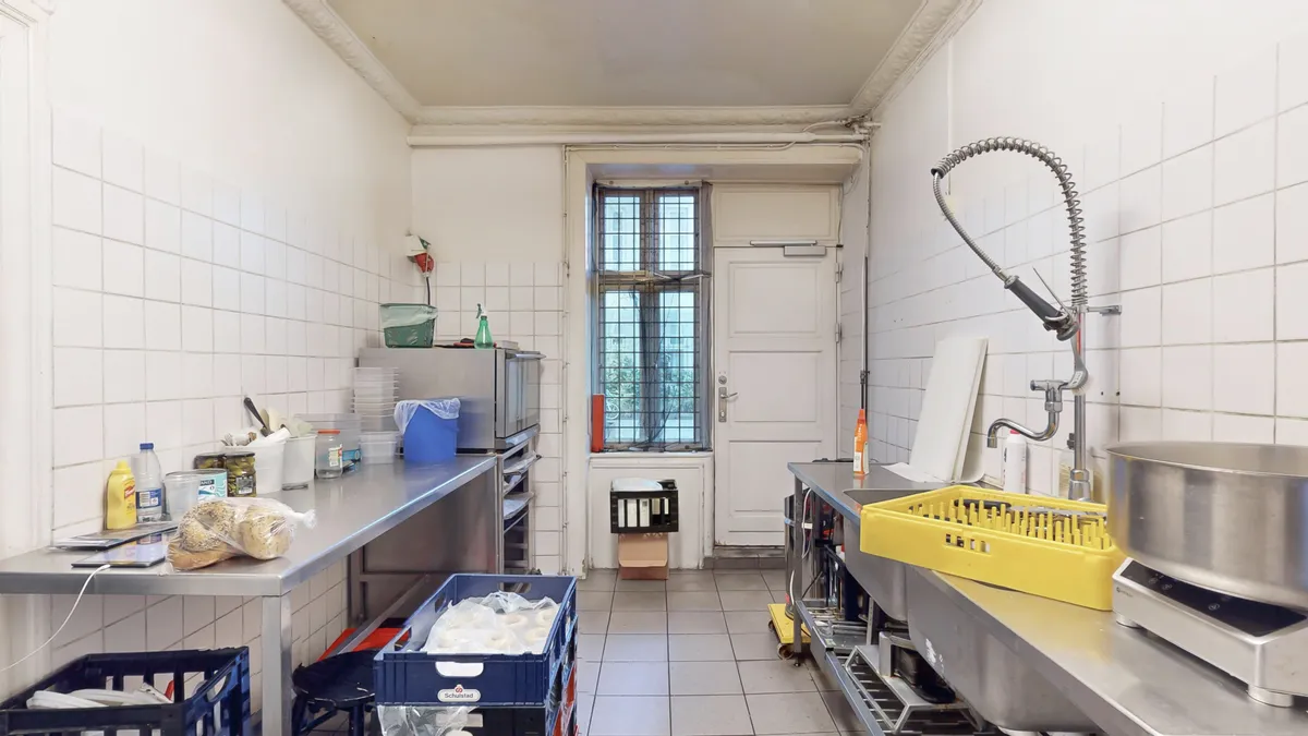 Lejet koldt køkken med bord, mikrobølgeovn, køleskab og flere opbevaringskurve. Skurvægge og gulv. Sink og stålkøkken med bøjler og stålfade.