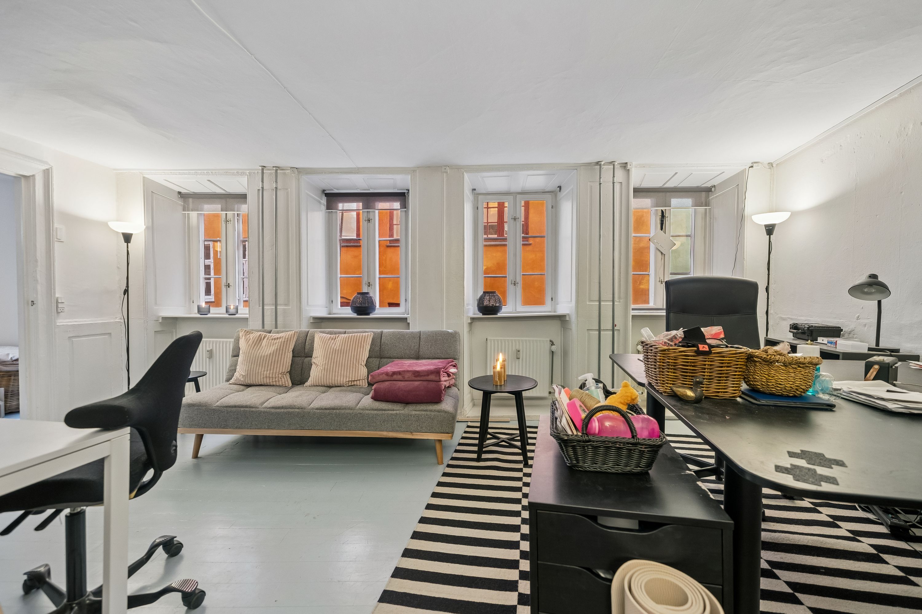 Kontor med skrivebord, sofa, to stole, to lamper og fire vinduer på Hyskenstræde 16A, 1. sal i København K.