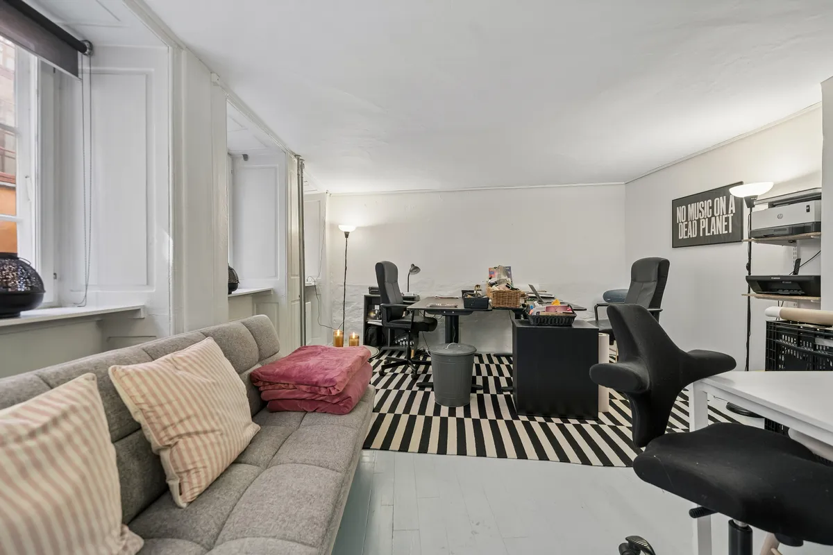 Kontor med sofa og skrivebord i det lyse og rummelige lokale med hvide vægge og sort-hvide gulvbelægning samt minimalistisk indretning
