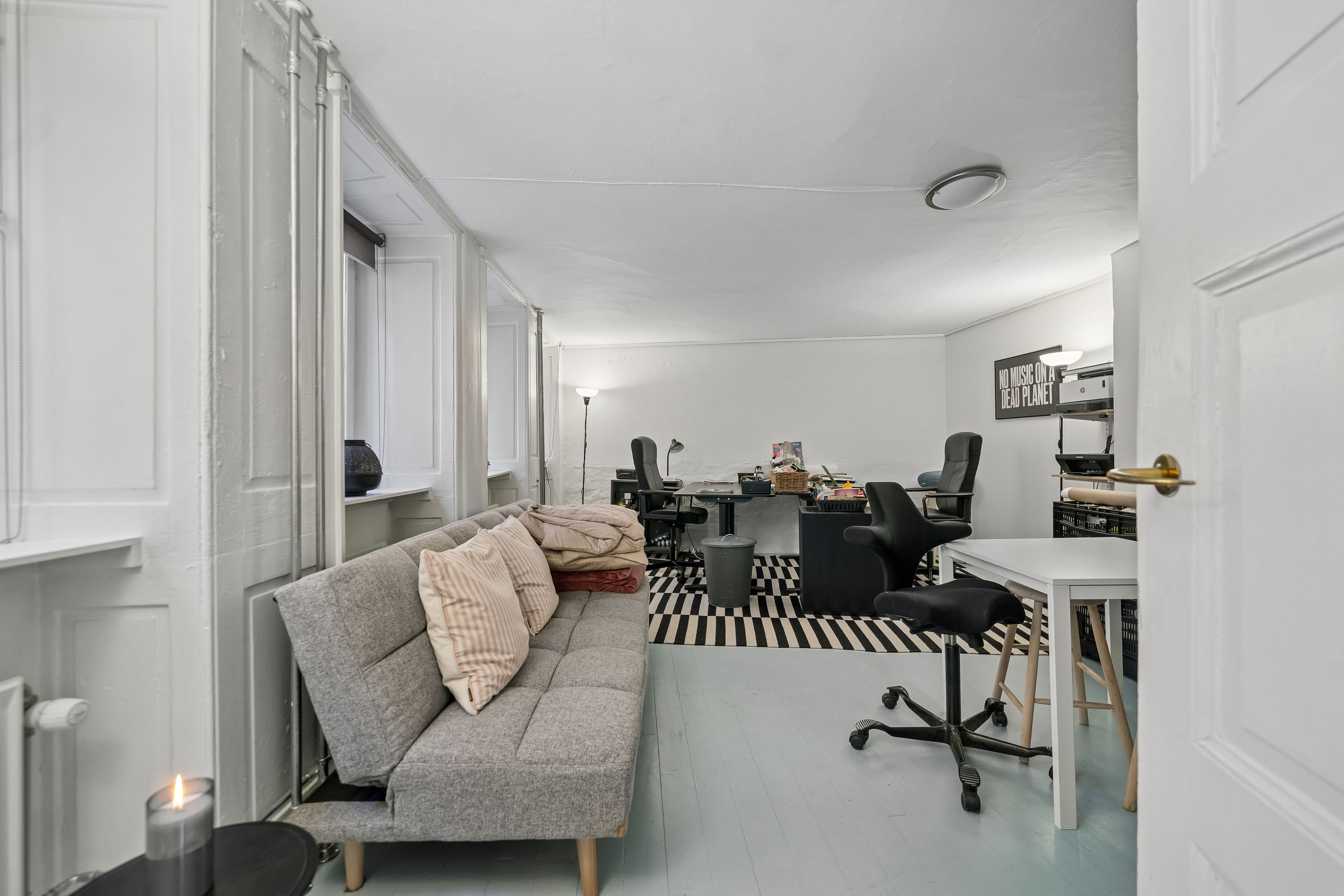 Kontor med lyse lofter og moderne møbler, sofa, skrivebord, bordlampe og flere kontorstole i sort og hvidt. Plakat med teksten "No music on a dead planet"