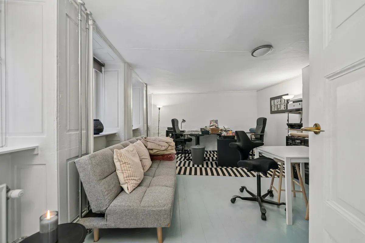 Kontor med lyse lofter og moderne møbler, sofa, skrivebord, bordlampe og flere kontorstole i sort og hvidt. Plakat med teksten "No music on a dead planet"