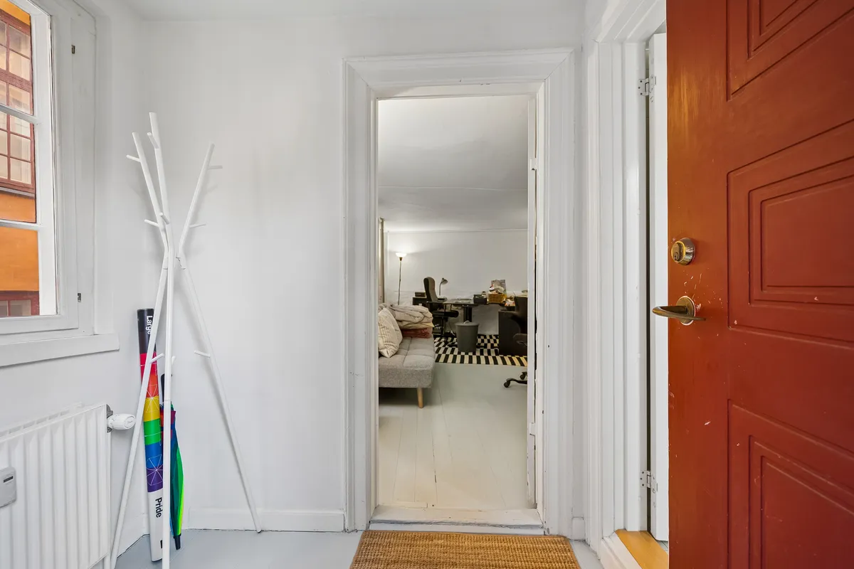 Københavnsk kontor med åben dør og lysegule vægge, hvidt tøstang, sofa og skrivebord med bøjle til paraplyer og regnfrakker.