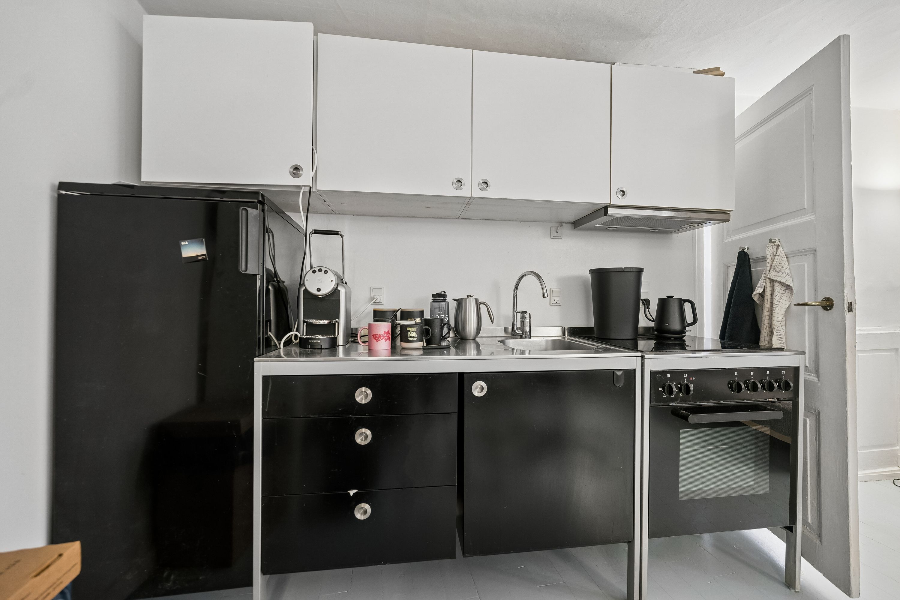 Hjørnekontor med hvide vægge, moderne møbler, sort køleskab, skabe og gulv, lysegrå loftsloft og lysegrå gulvbelægning