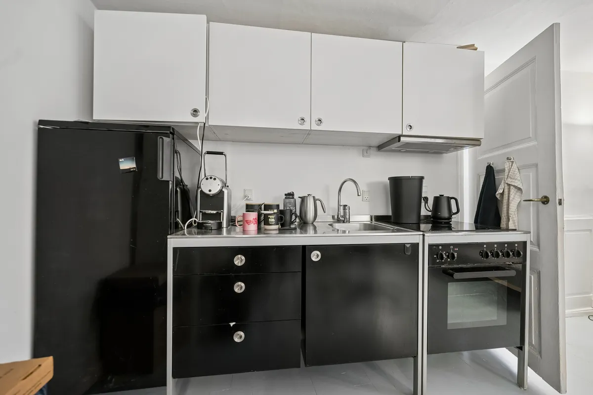 Hjørnekontor med hvide vægge, moderne møbler, sort køleskab, skabe og gulv, lysegrå loftsloft og lysegrå gulvbelægning