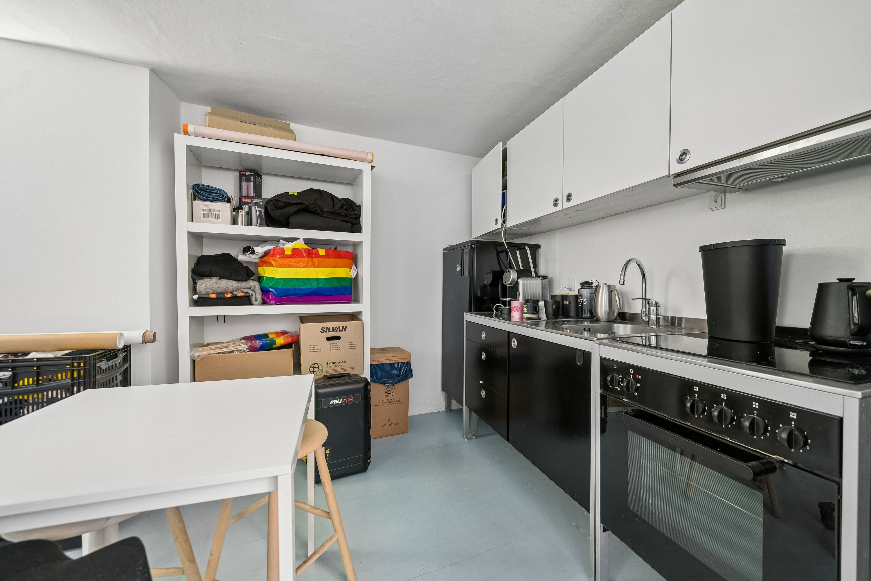 En lille køkken med hvidt bord, ståhøj bar og hvide skabe med lysegrå loftsgulve og lysegrå vægge med lysegrå loft.