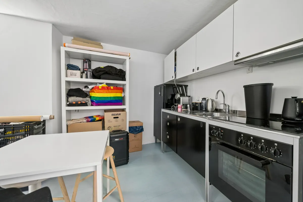 En lille køkken med hvidt bord, ståhøj bar og hvide skabe med lysegrå loftsgulve og lysegrå vægge med lysegrå loft.