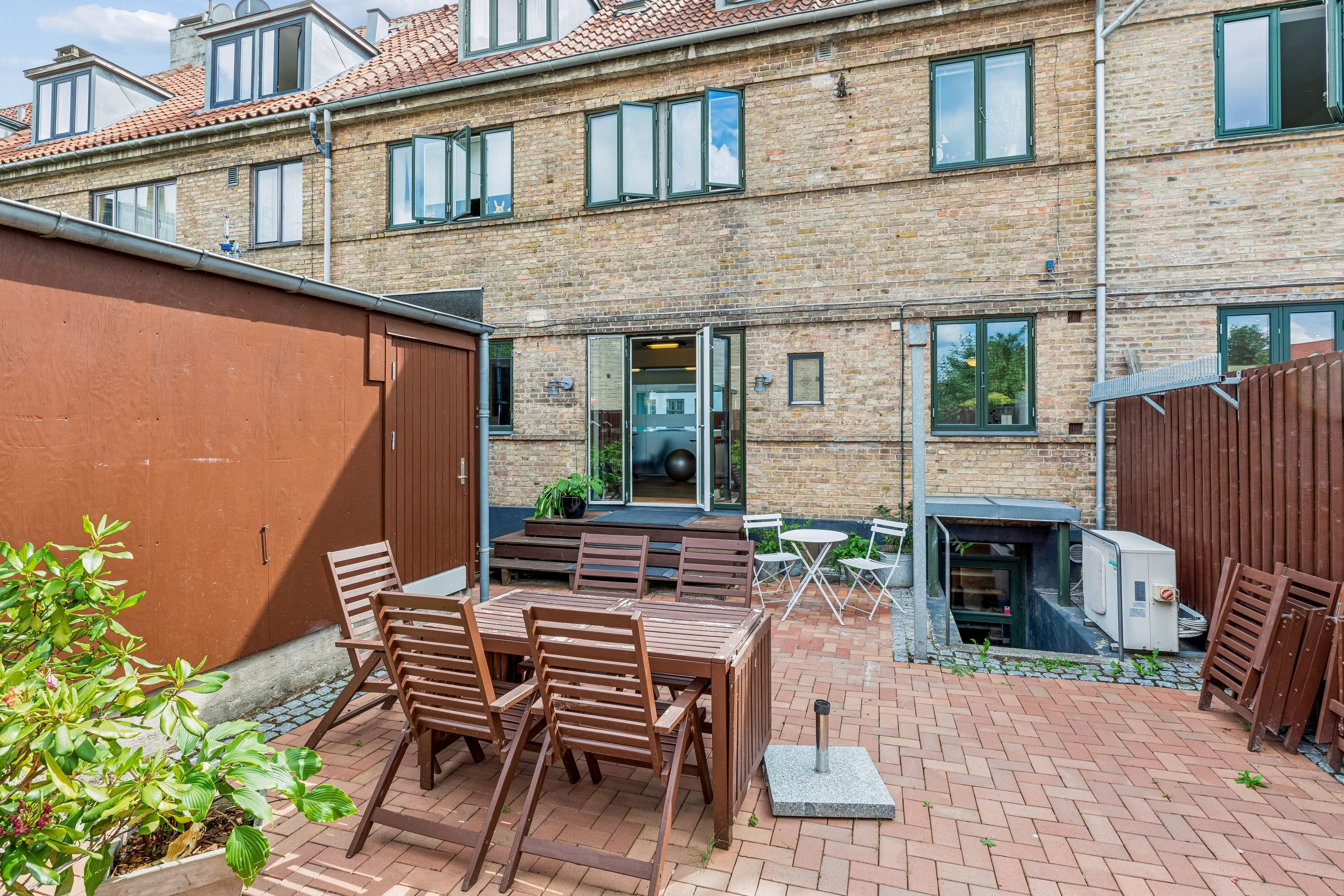 Lejlighed med terrasse på Godthåbsvej, Frederiksberg. Træbord med stole og plante samt kælderadgang og garage.