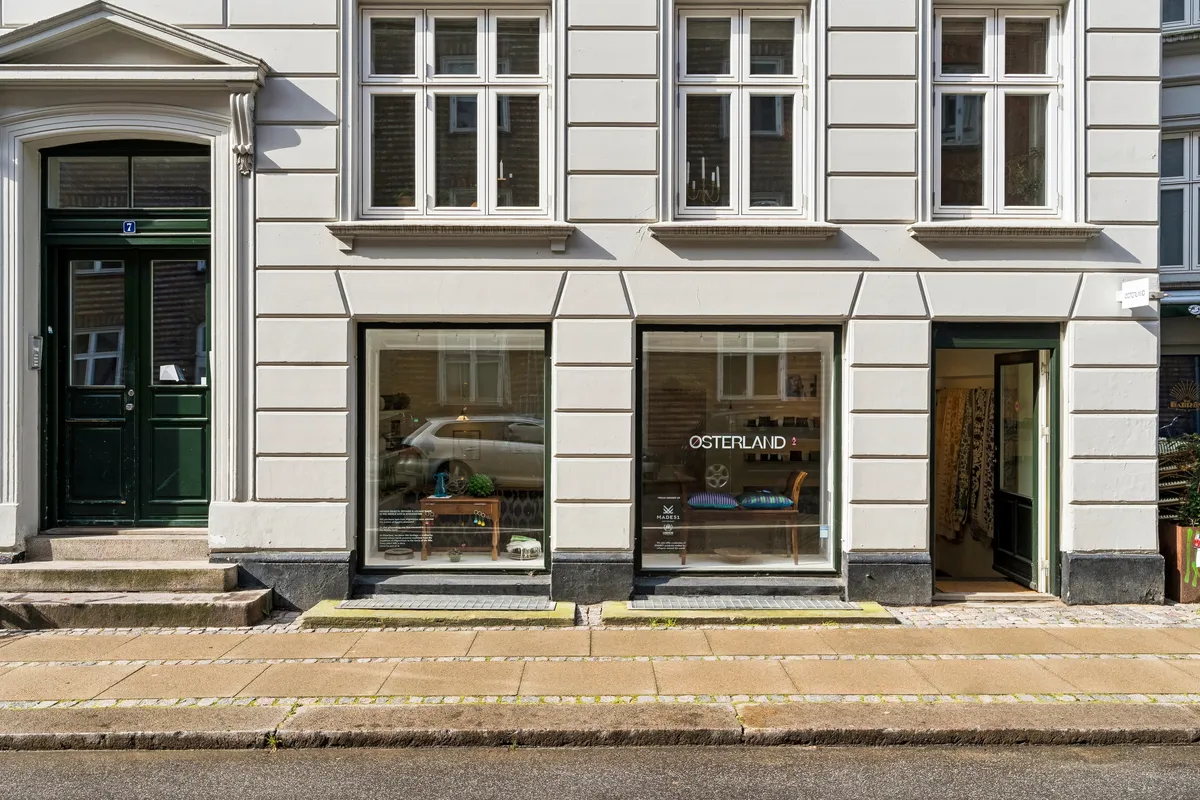 Kontor til leje på Egegade 7 i København. Tre separate butikslokaler med indgange og vinduer. Indvendigt møbler og plantepotte. Brandplade hængende udenfor.
