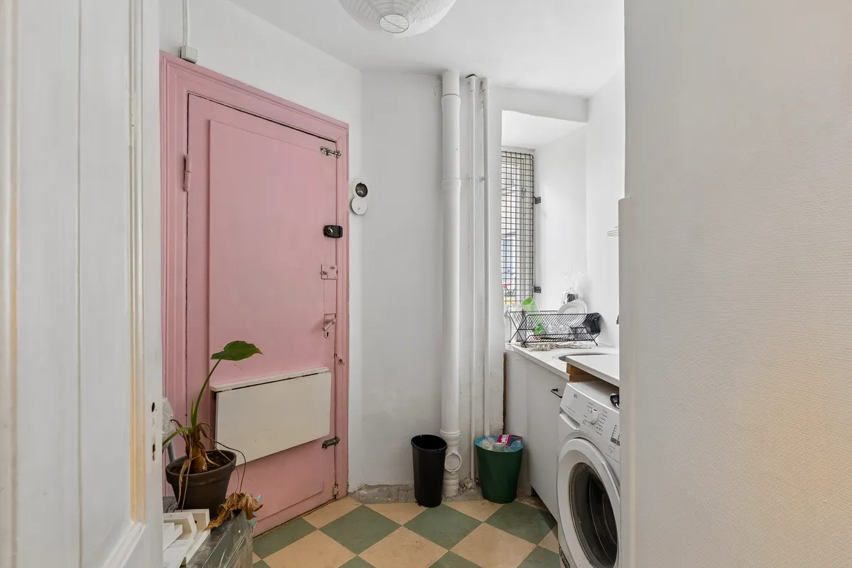 Pink dør til lejlighed med tøjvask i baggrunden og plastikposer og plante foran døren