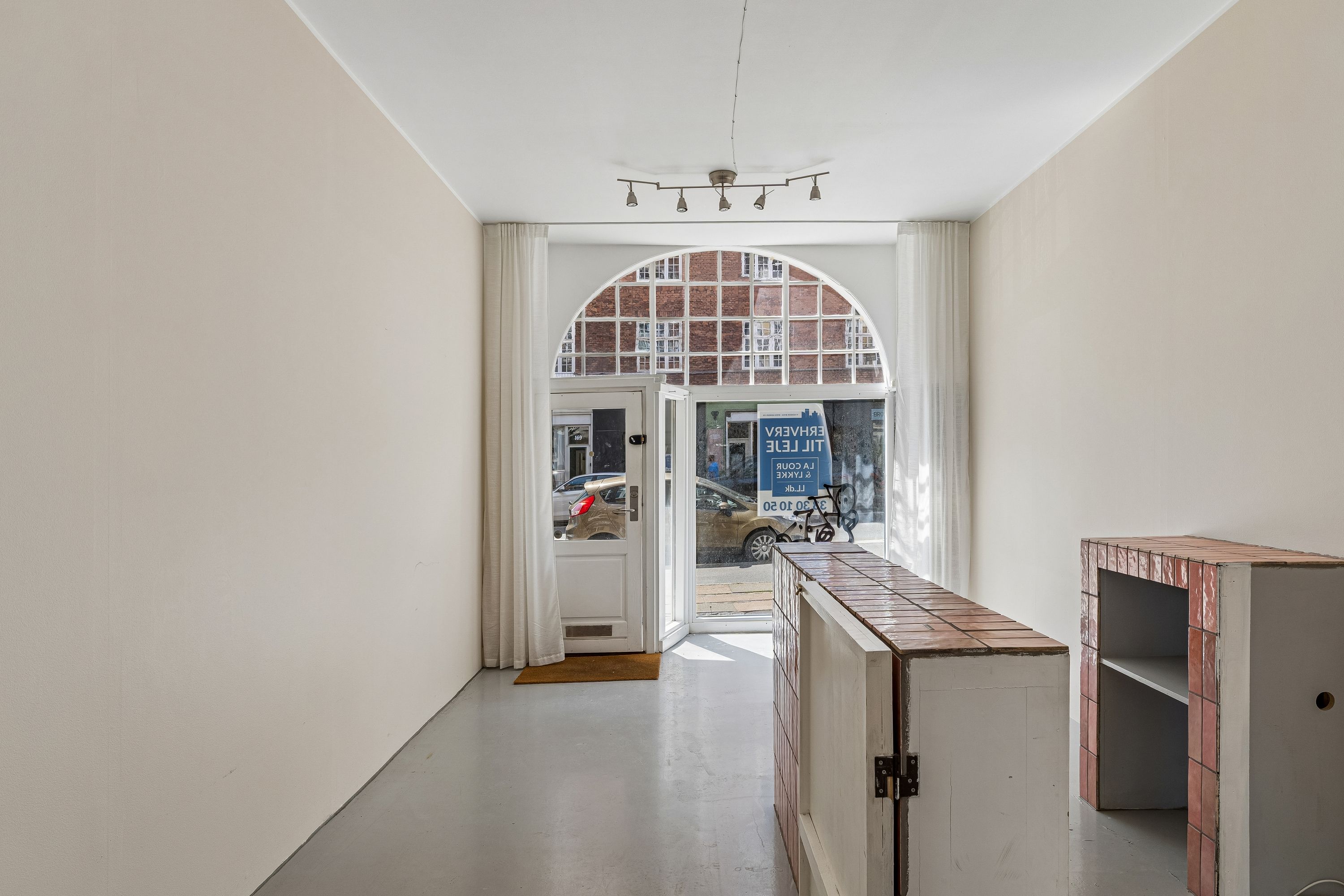 Store glasruder og lysegule vægge i erhvervslokaler på Vesterbrogade 180, st. 1. Lyskroner hænger i loftet, og der er trægulv foran døren