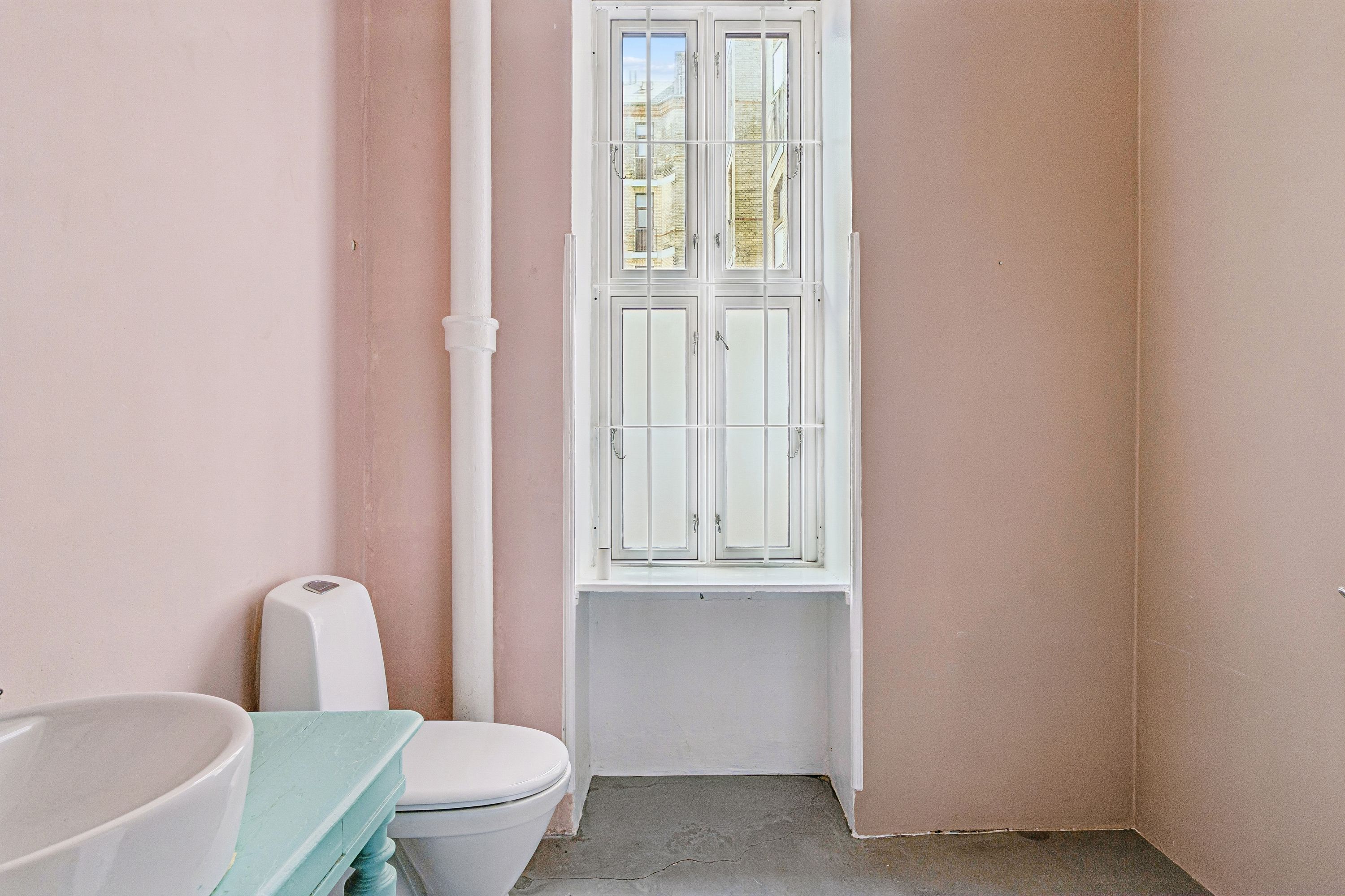 Lys, rent og pænt badeværelse med hvid toilet, hvidt vasketøjsbord, hvidt badekar og pinke vægge
