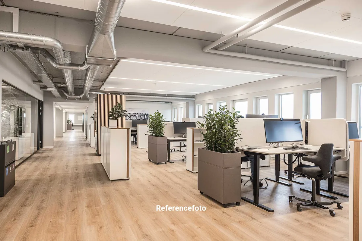 Kontorlokaler med lyse loftsvinduer og moderne møbler. Store plantepoter, ergonomiske stolpe og skærme til computere. Højt til loftet og trægulv.