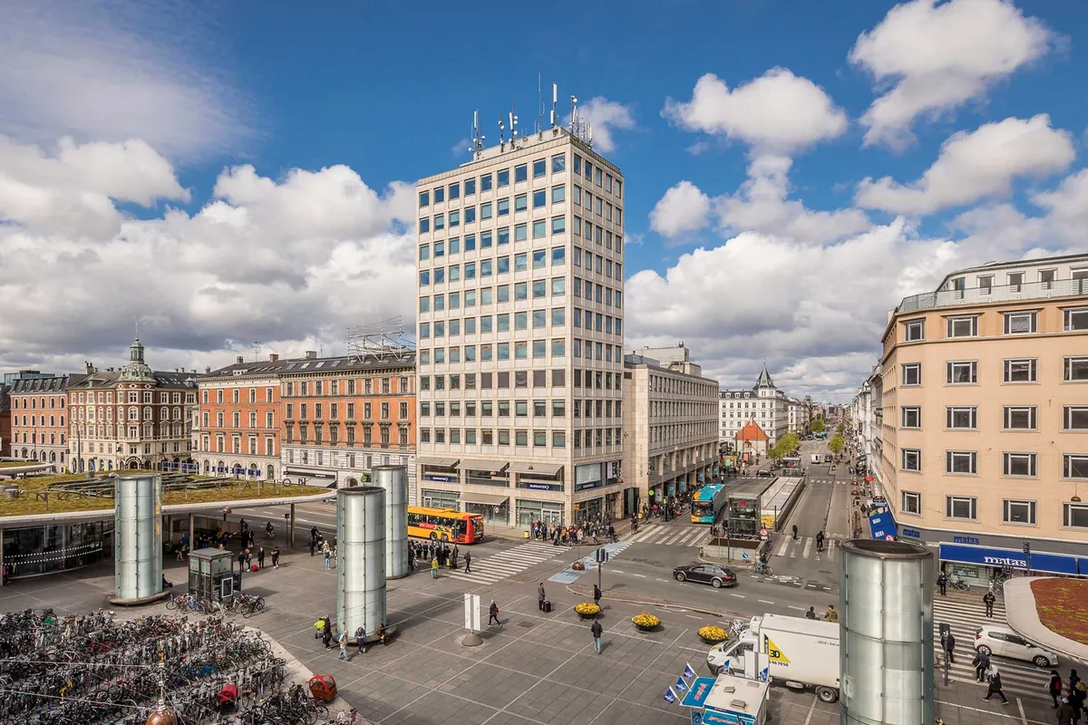 Moderne kontorbygning med mange vinduer og busser udenfor Nørreport Station, med mange fodgængere og parkerede biler