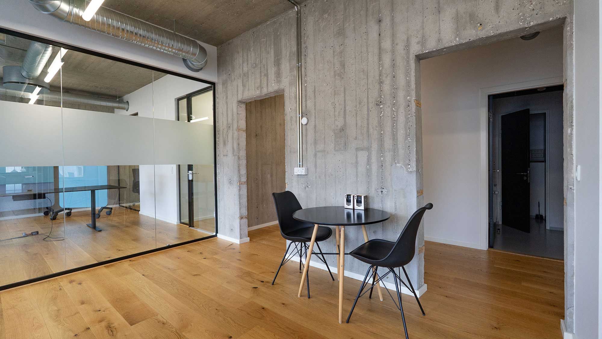 Modernt og rummeligt kontor med høje lofter, glasvinduer og møbler med en minimalistisk stil. Rundt borde med stol og høj kvalitet gulvbelægning.