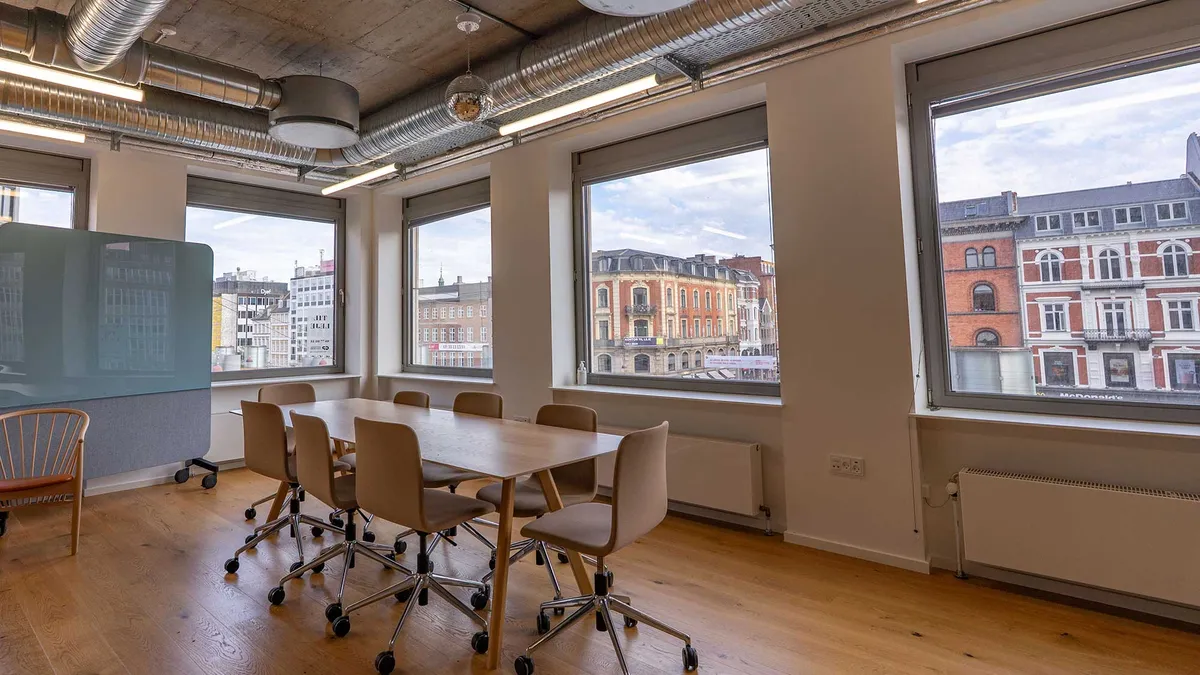 Kontorrum med moderne udsmykning og store vinduer, der giver udsigt til bygninger og skyerne