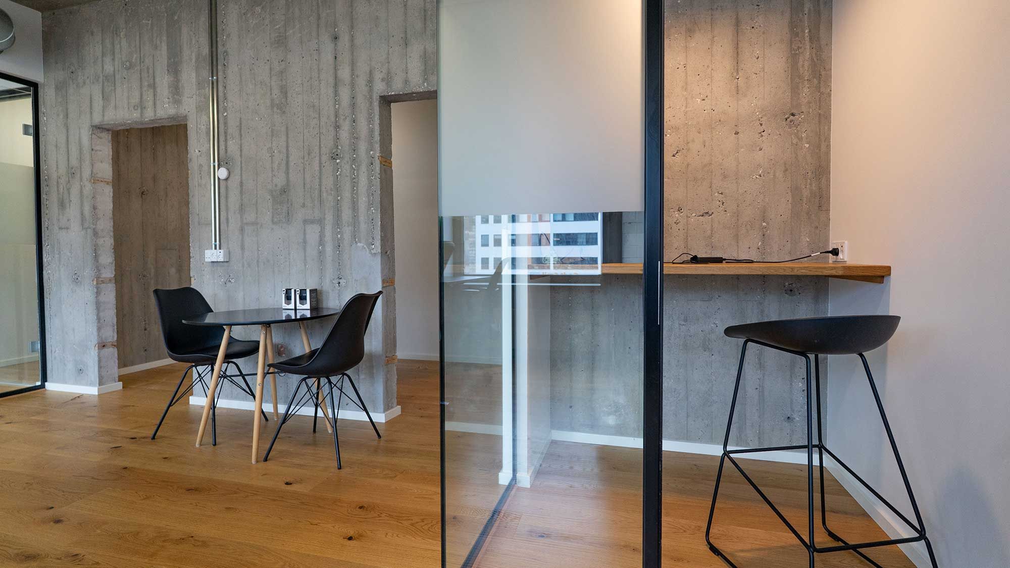 Kontor med moderne møbler og store ruder, to stole og et bord samt en høj barstol