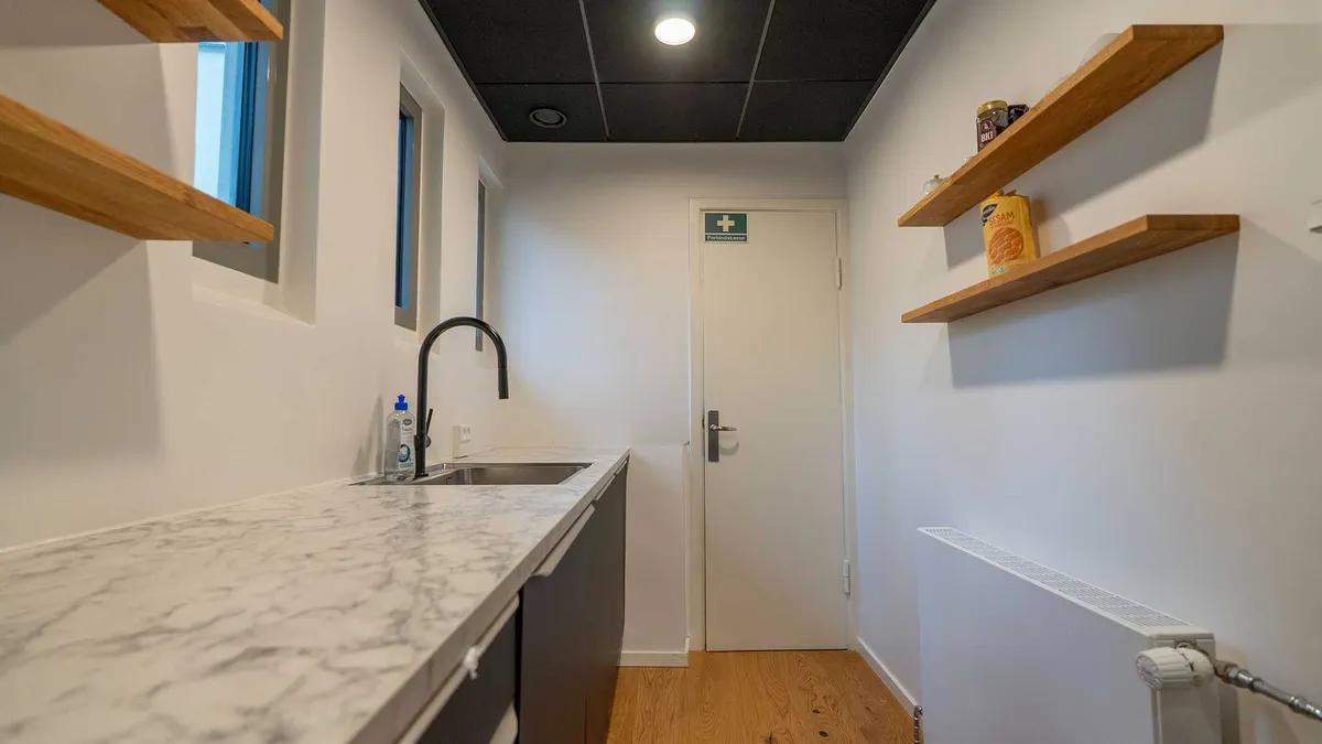 Lyst og rent kontorlokal med hvidt marmor gulv og marmor køkkenbord, to højre hængende hylder og to små vinduer med udsigt til Nørreport Station