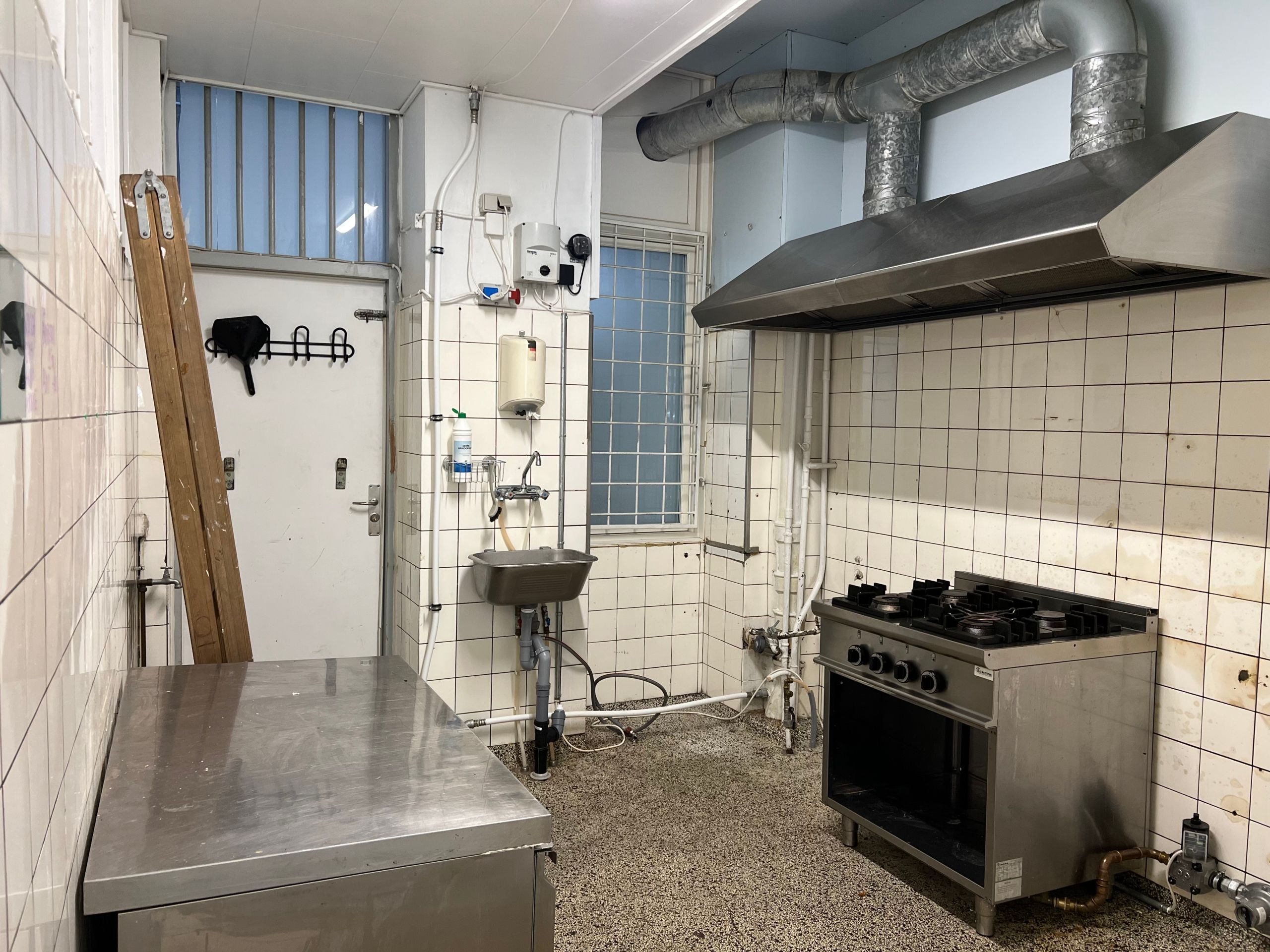 Take-away køkken med spisestue, ovn og gaskomfur samt metalbord og metalskab. Væggene er hvide og udstyret med røre og slibe.