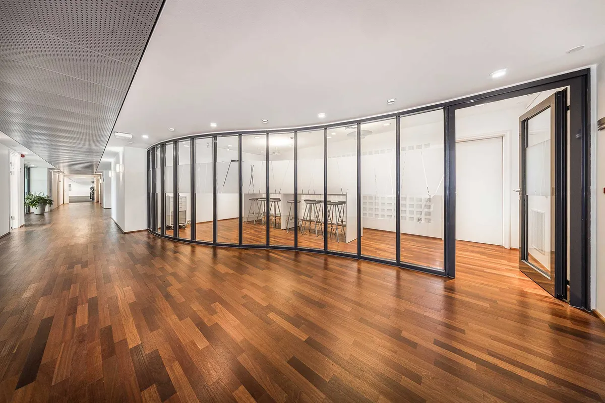 Kontorbygning med højloft, hjørneglasvægge og møbelsæt med barstole. Massiv trægulv og gule væglampe. Rundt gulvdesign og hvidt loft.