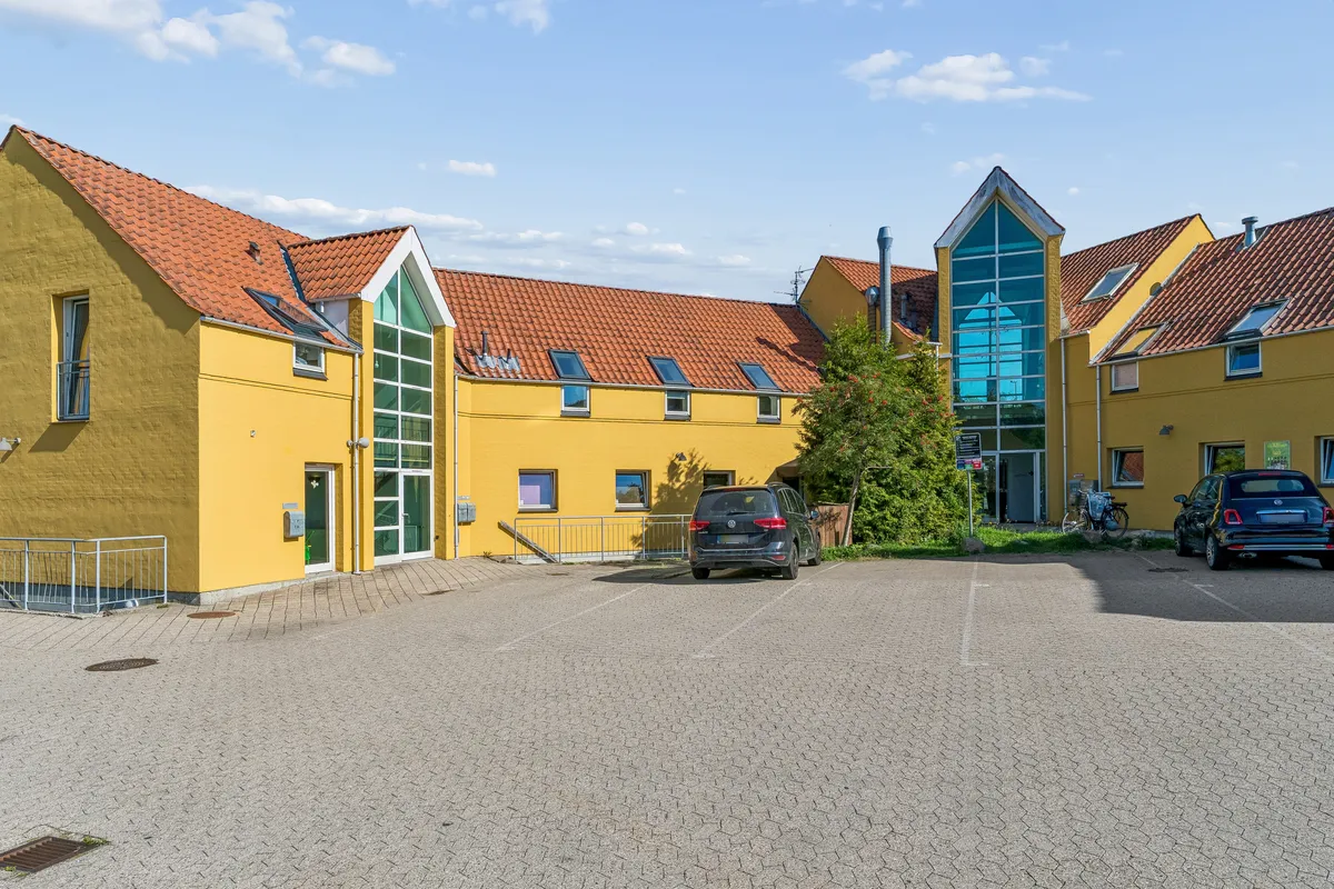 Et smukt, gult hus med røde tag og glasvinduer med parkeringsplads og to parkerede biler foran