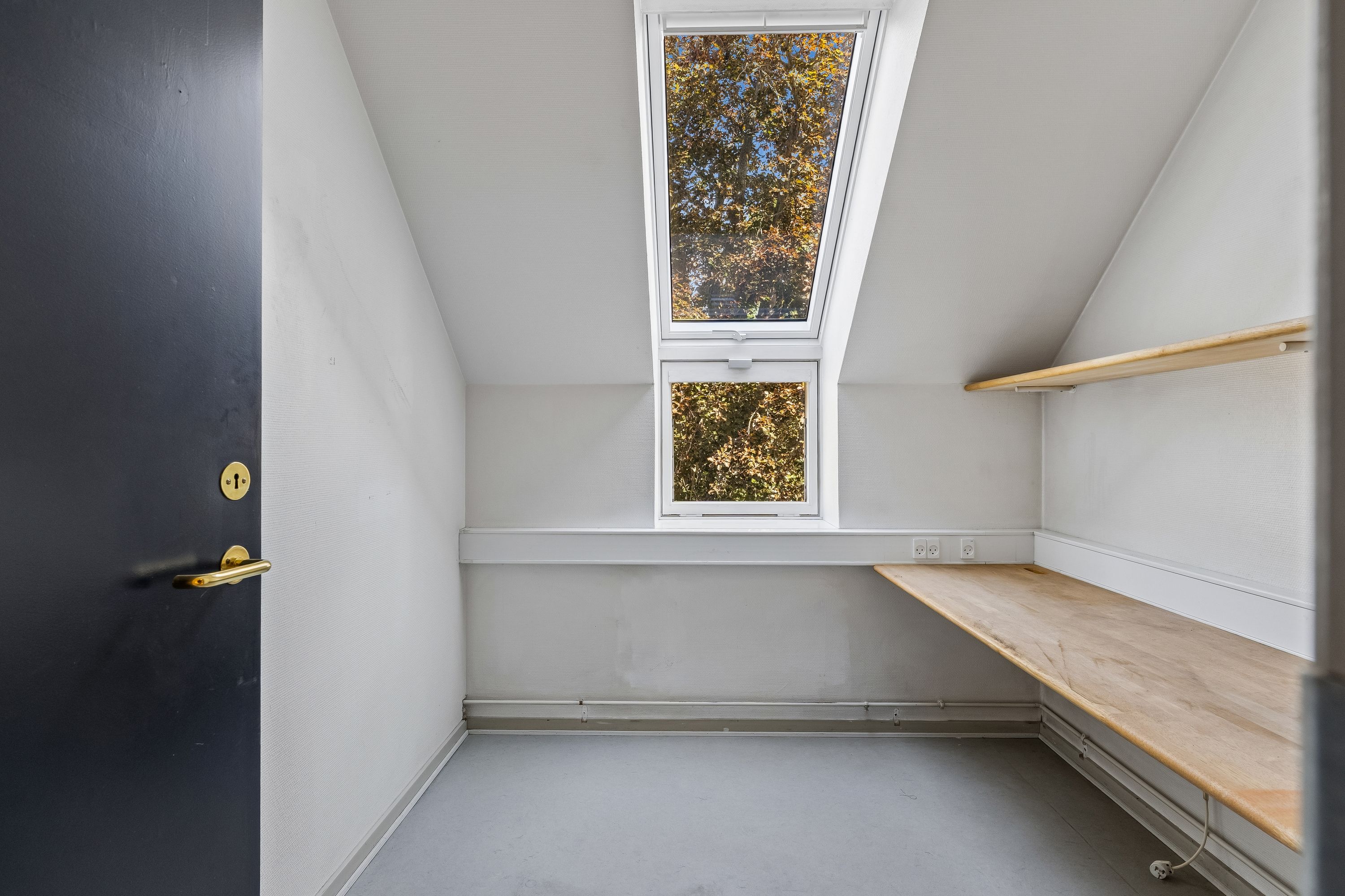 Et rum med to vinduer, en loftsvindu og en skrånende væg, hvor der er et brædt stel med to højttalere og en indbyggede stikkontakter